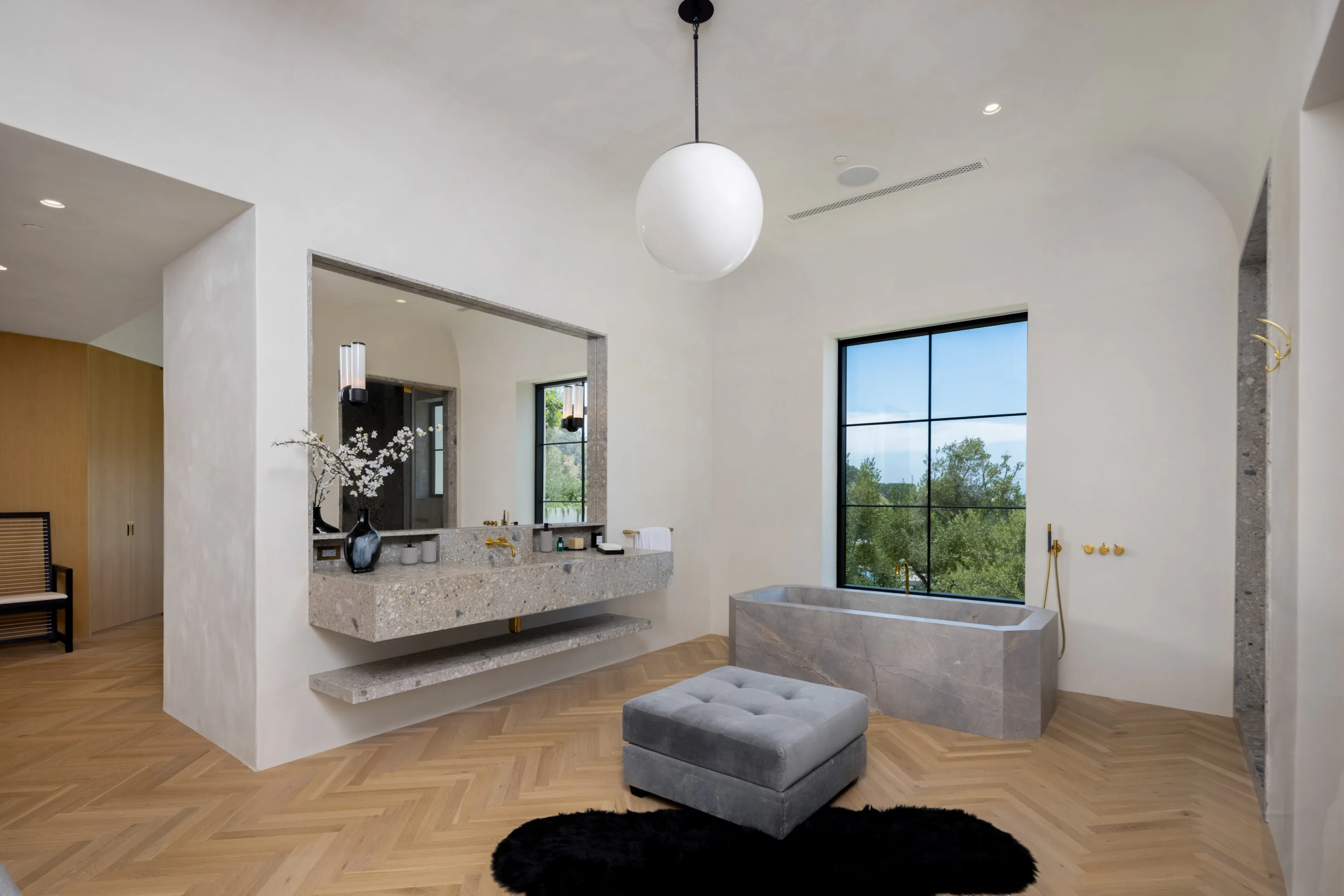 Guest bath with stone trough tub, floating terrazzo vanity and tall window onto greenery