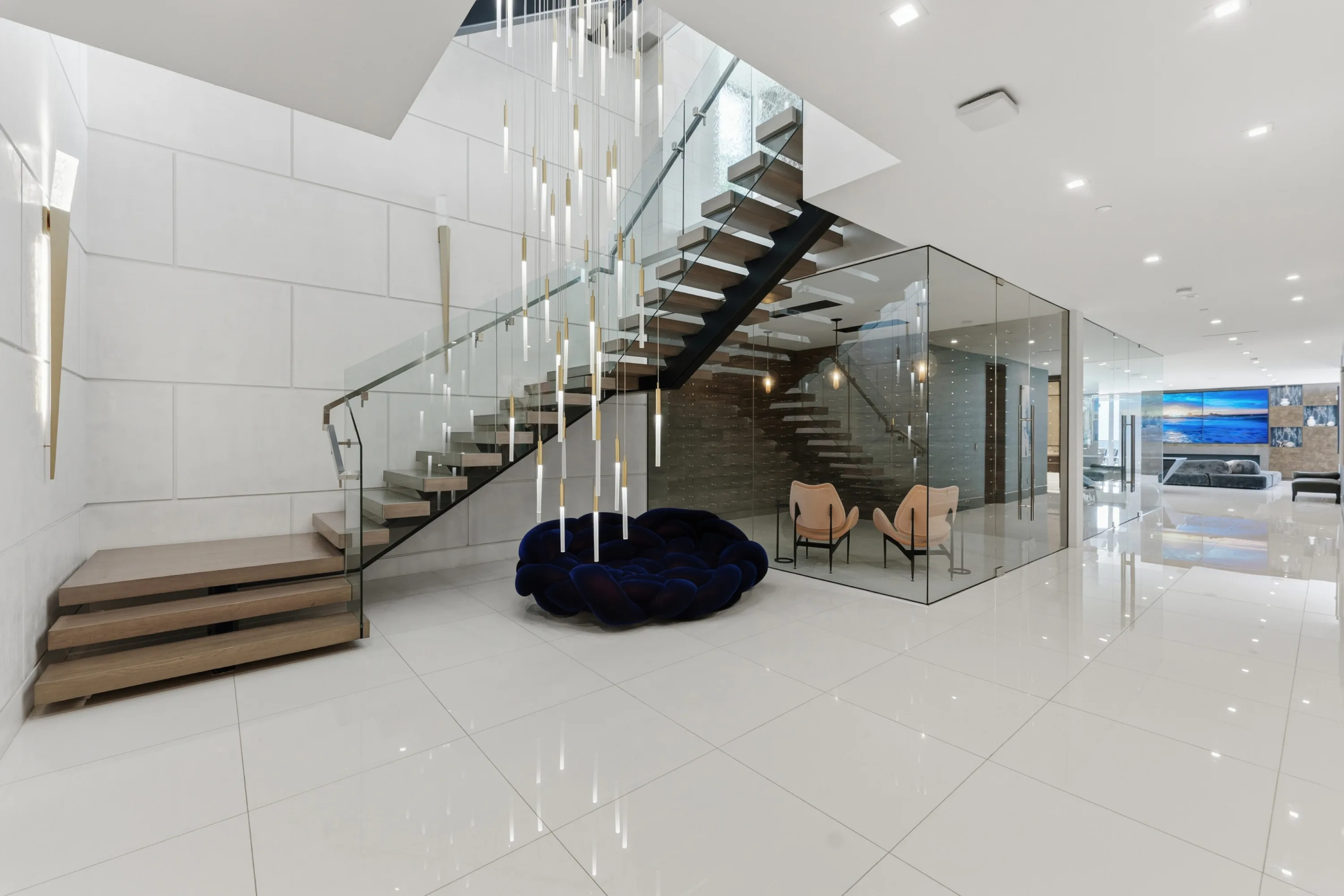 Double-height entry hall with floating staircase, cascading glass-rod chandelier and glass-walled sitting room