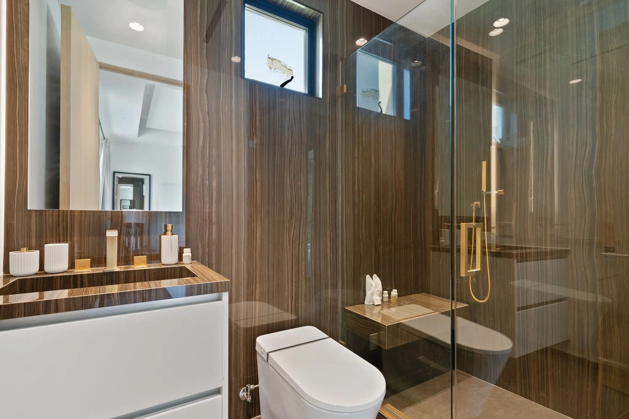 Ensuite shower room panelled in dark figured stone with brass fittings and glass enclosure