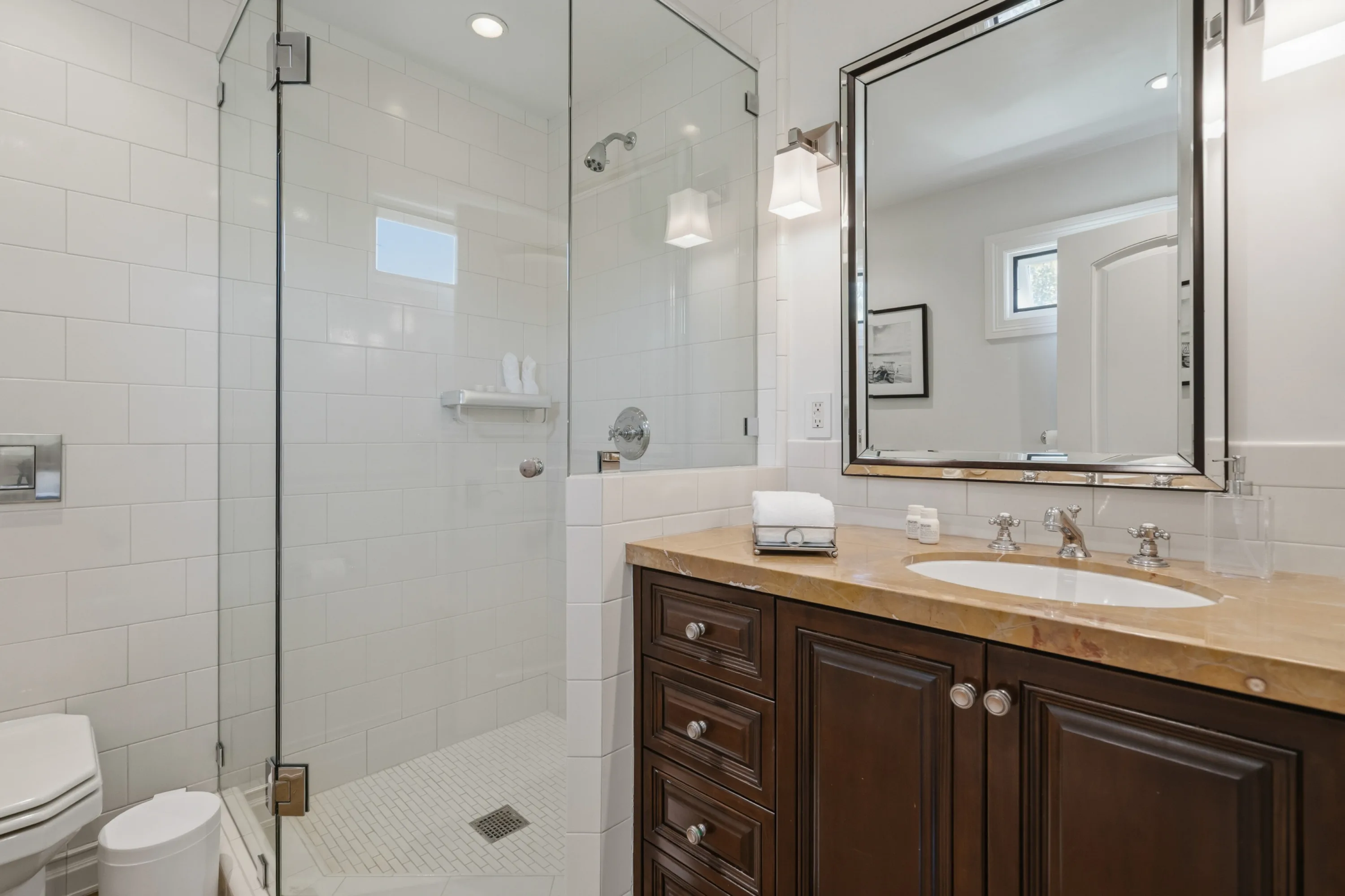 En suite shower room with subway-tiled glass shower and honey-toned stone vanity