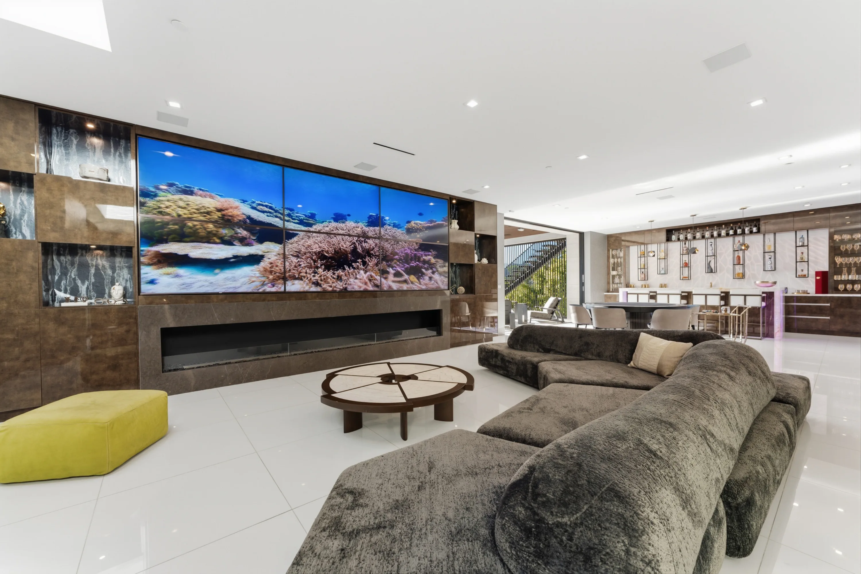 Lower lounge with plush sectional, linear fireplace and a video wall running to the far bar