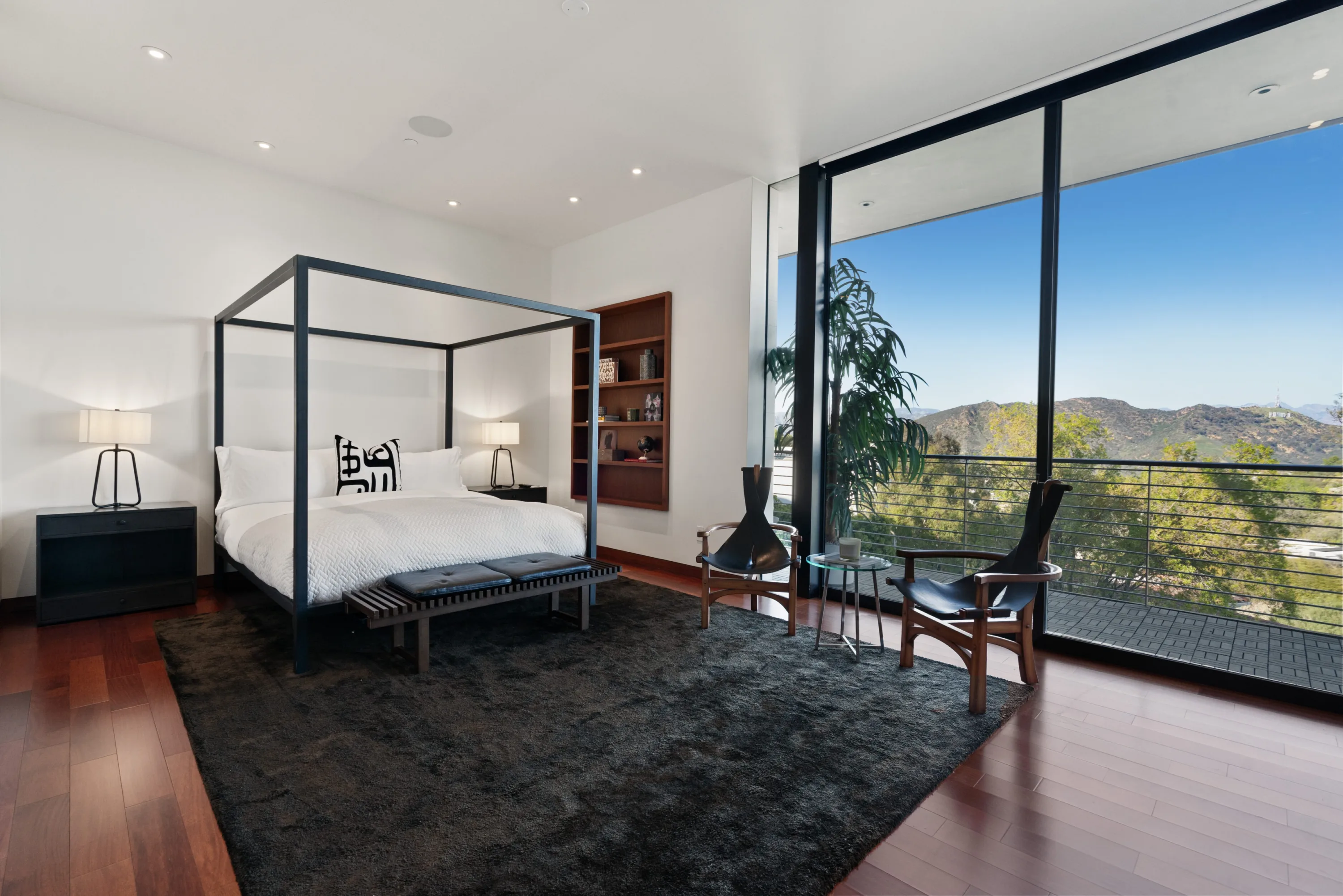 Primary suite with four-poster bed, leather armchairs and floor-to-ceiling glass onto the canyon