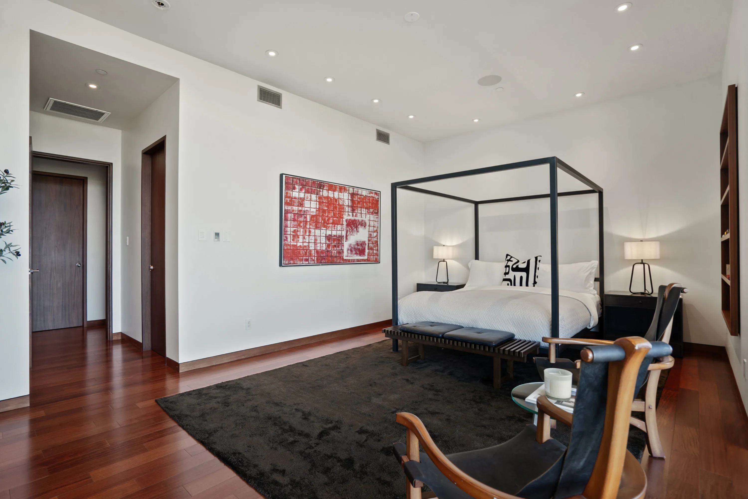 Wider angle of the primary suite showing red abstract canvas and seating area on dark rug