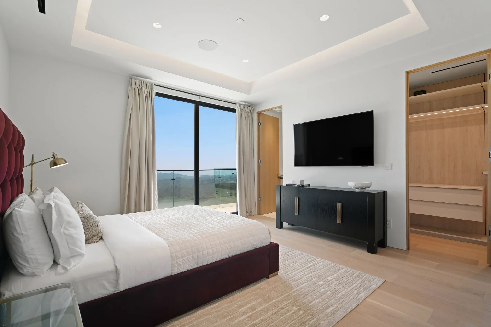 Bedroom with deep burgundy bed, slider onto a canyon-view balcony and lit walk-in wardrobe