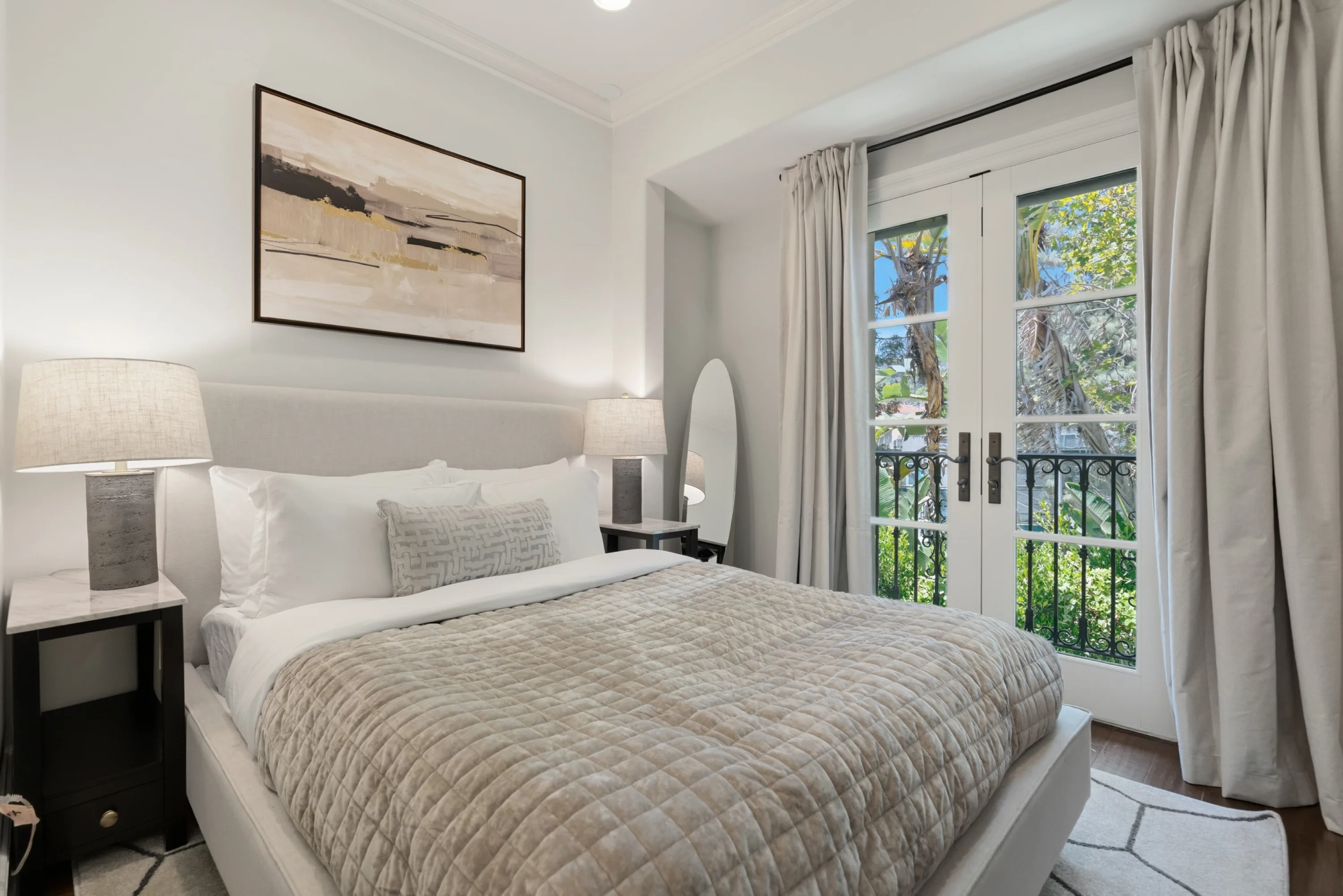 Smaller guest bedroom with quilted throw, abstract canvas and French doors framing palms