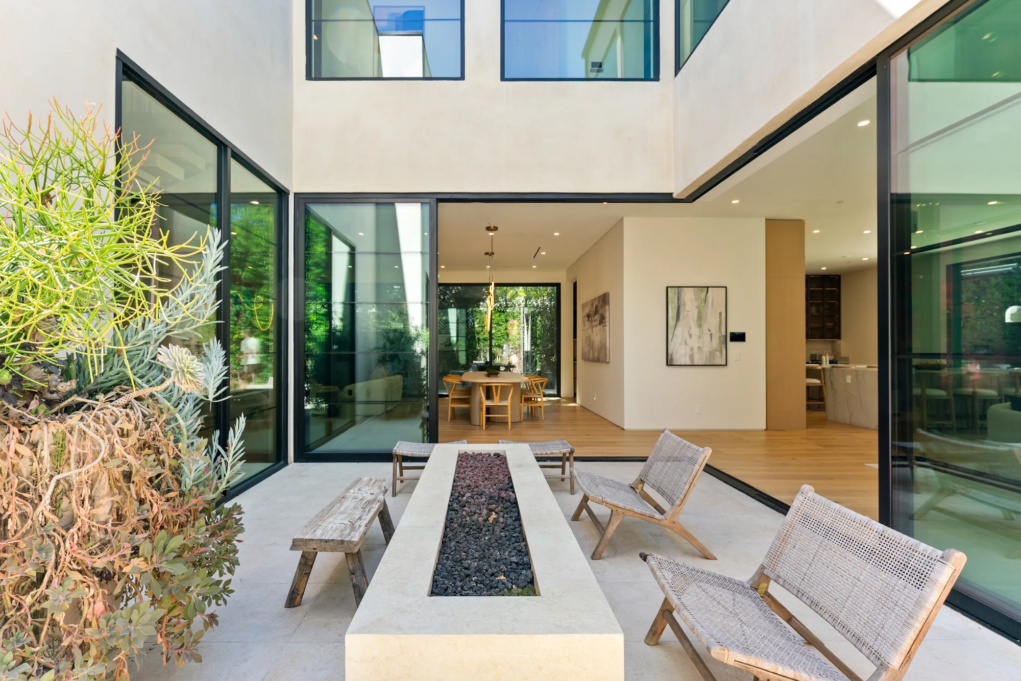 Double-height entry courtyard with linear fire table, woven lounge chairs and glass walls onto the dining room