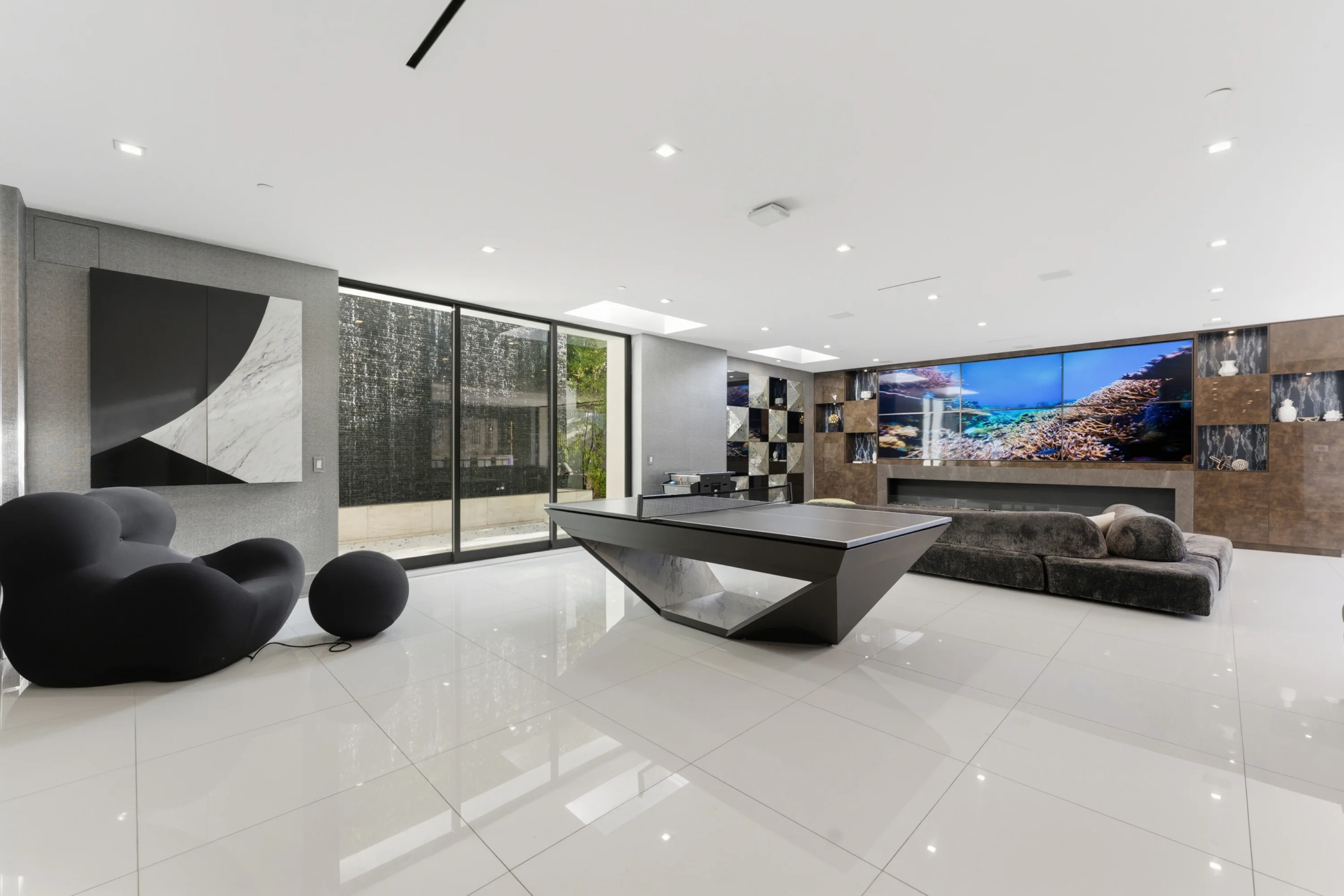 Games room with designer ping-pong table, sculptural black seating and water feature beyond the glass