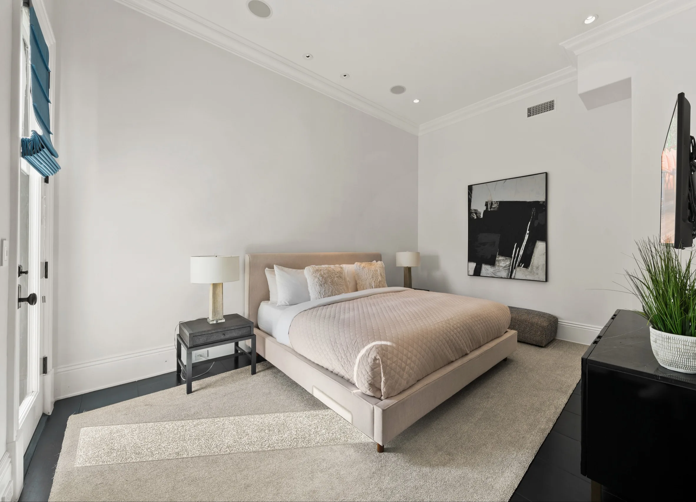 Minimal bedroom with blush quilted bed, abstract canvas and pale layered rug on dark floors