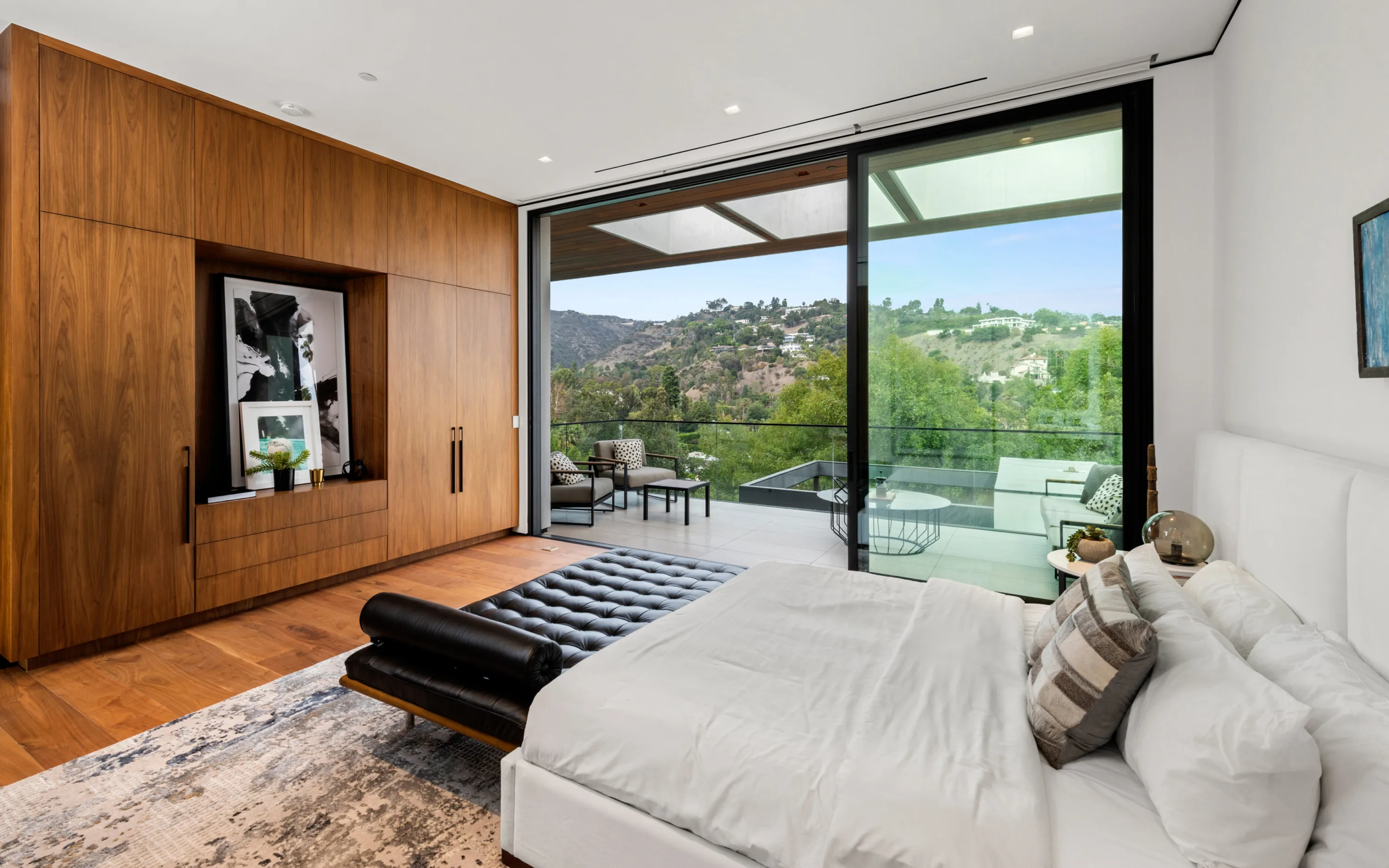 Bedroom sliding open to a private terrace with lounge seating and canyon outlook, tufted leather bench at the bed