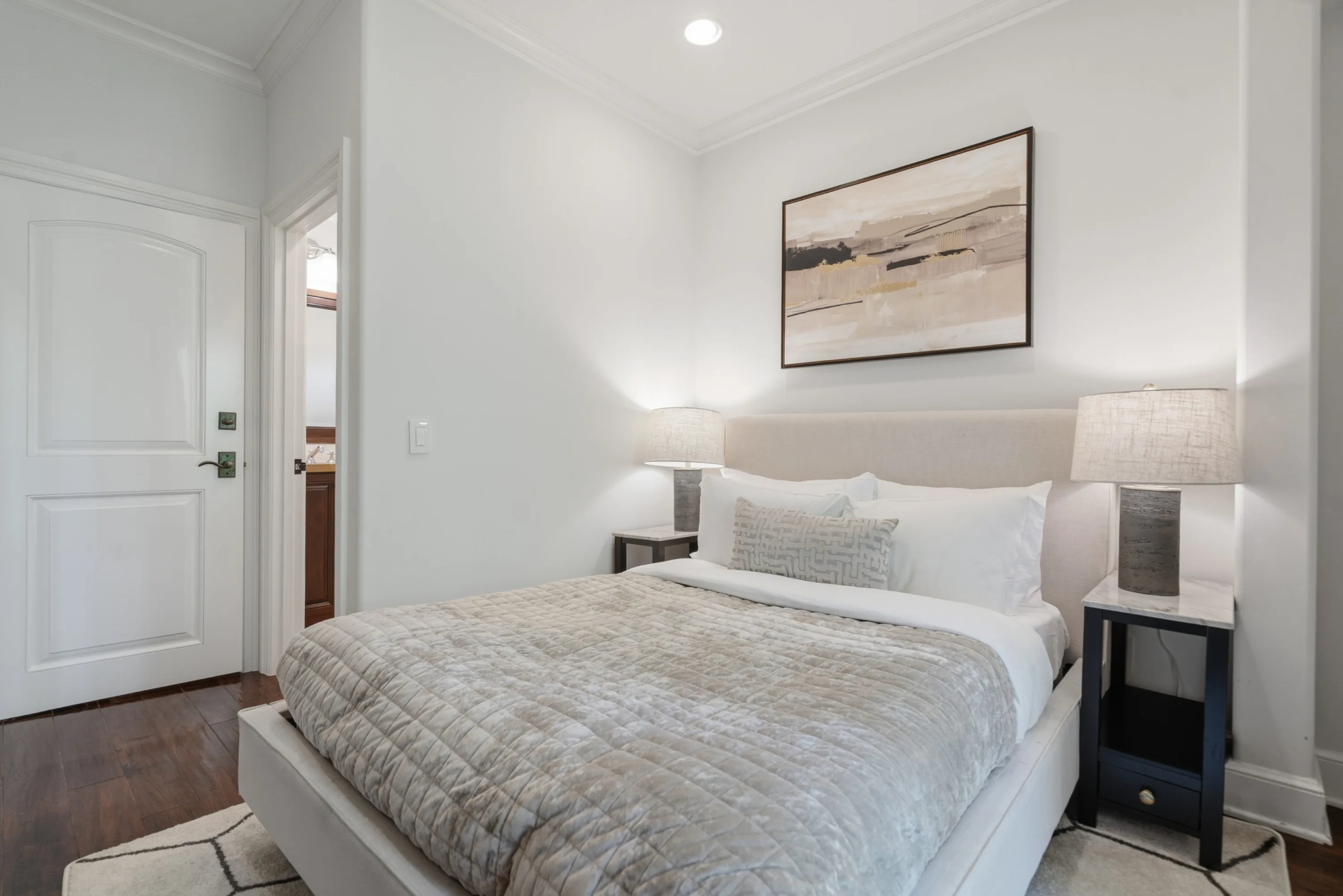 Guest bedroom with upholstered bed, quilted throw, twin ceramic lamps and abstract canvas above the headboard