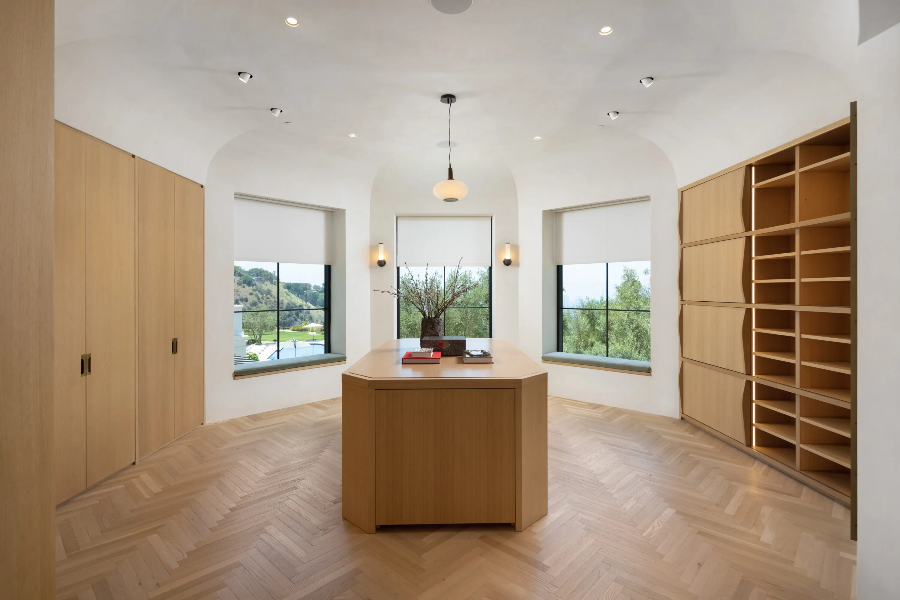 Oak-lined closet room with central island and arched windows over the lawn and pool