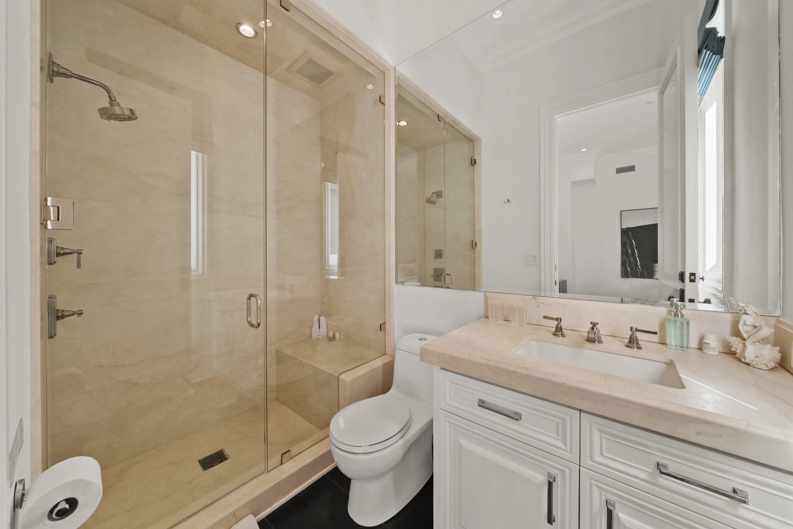 Compact guest shower room in warm cream stone with frameless glass enclosure