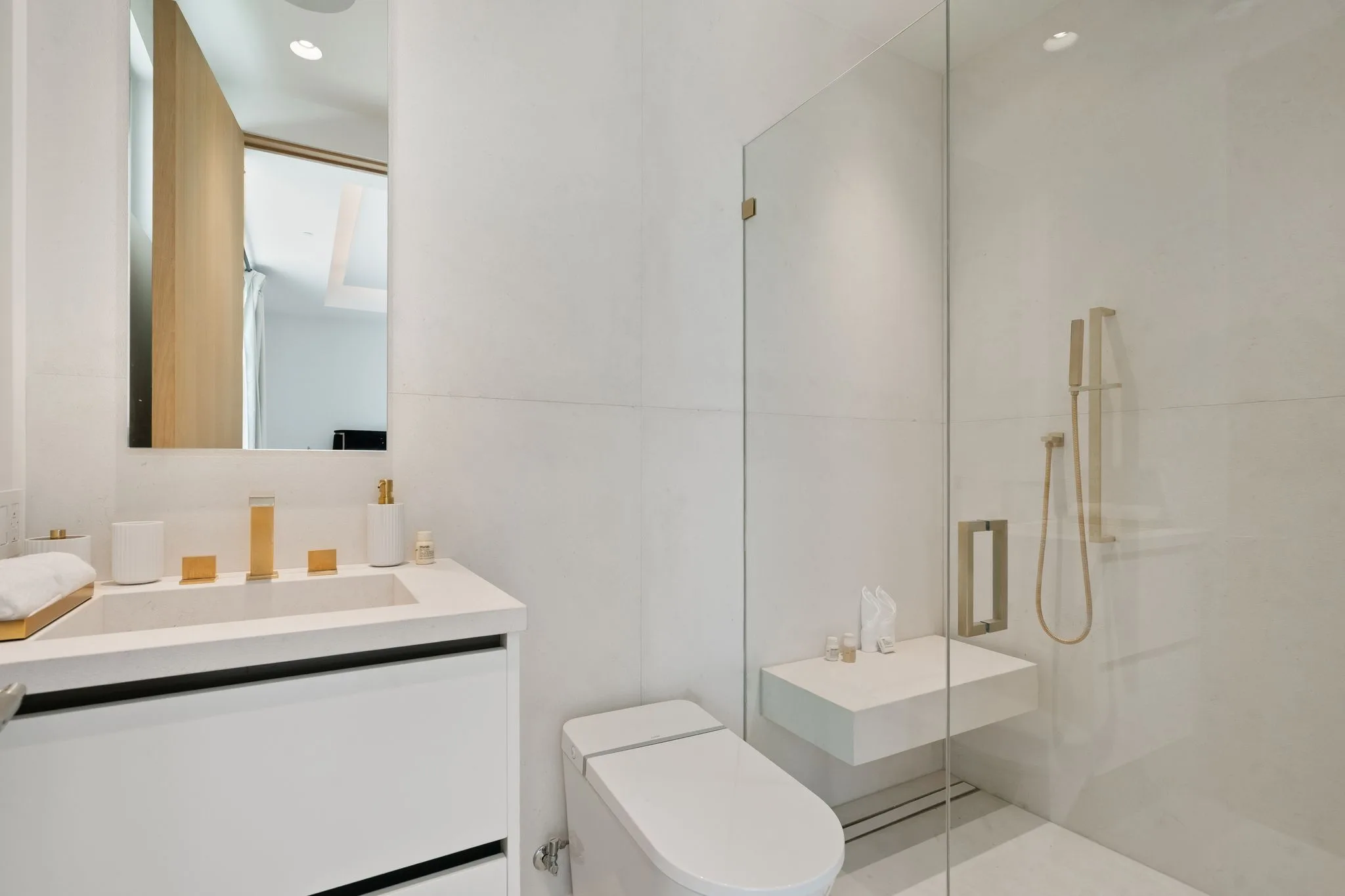 Compact guest bathroom in pale stone with brass tapware and a glass-screened walk-in shower