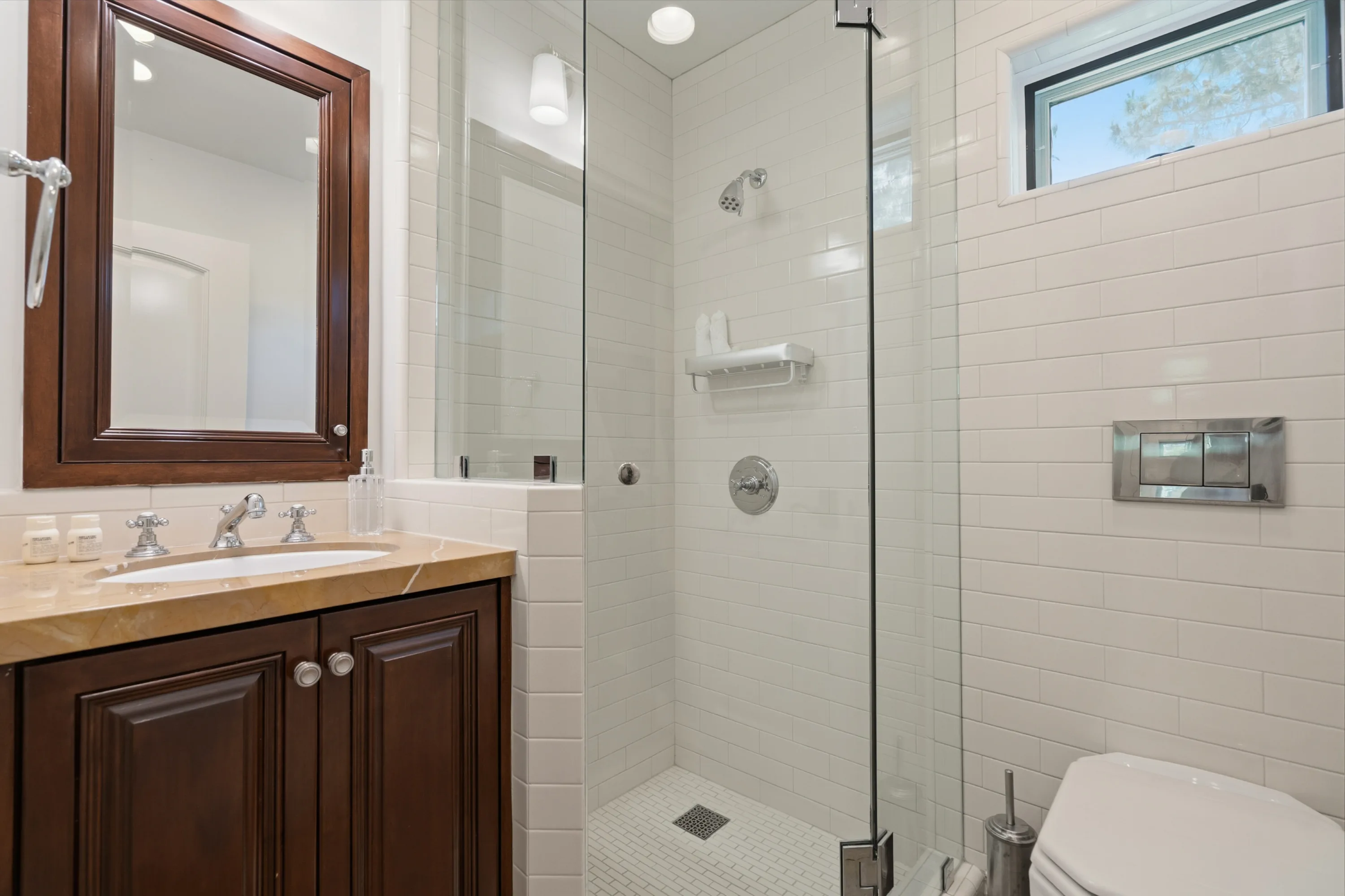 Ensuite bath with walk-in glass shower, white subway tile and a carved wood vanity under a matching mirror