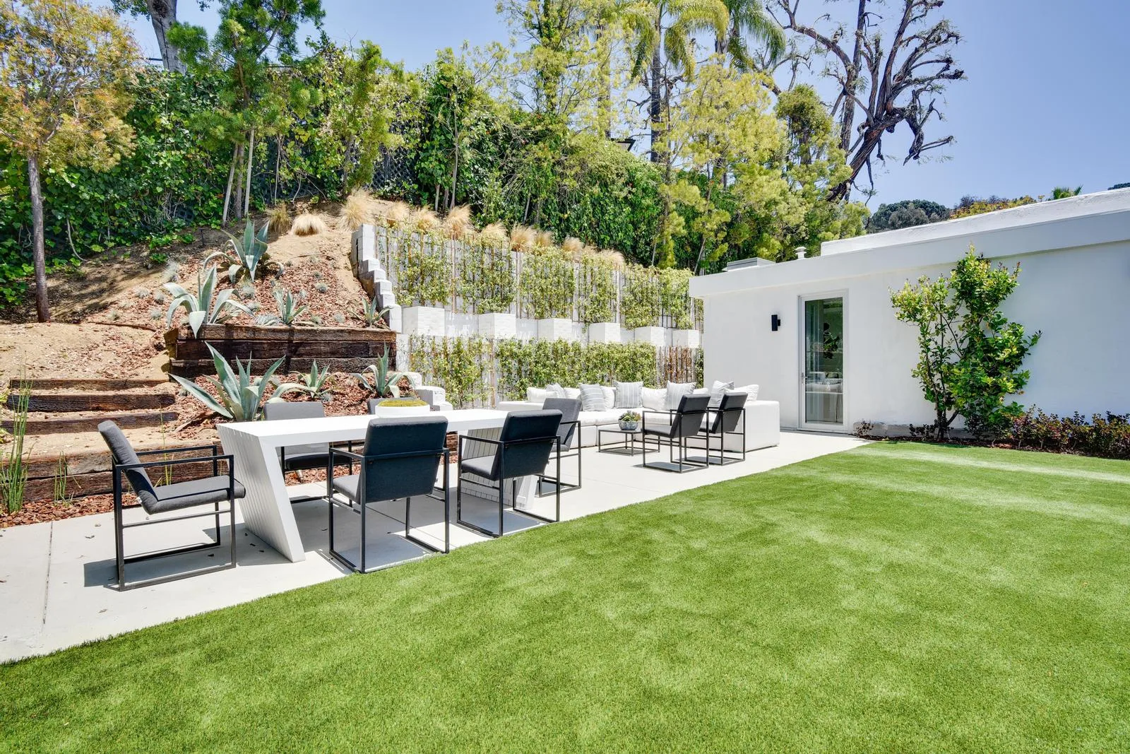 Outdoor dining and lounge patio edged by manicured lawn and a planted hillside of agaves