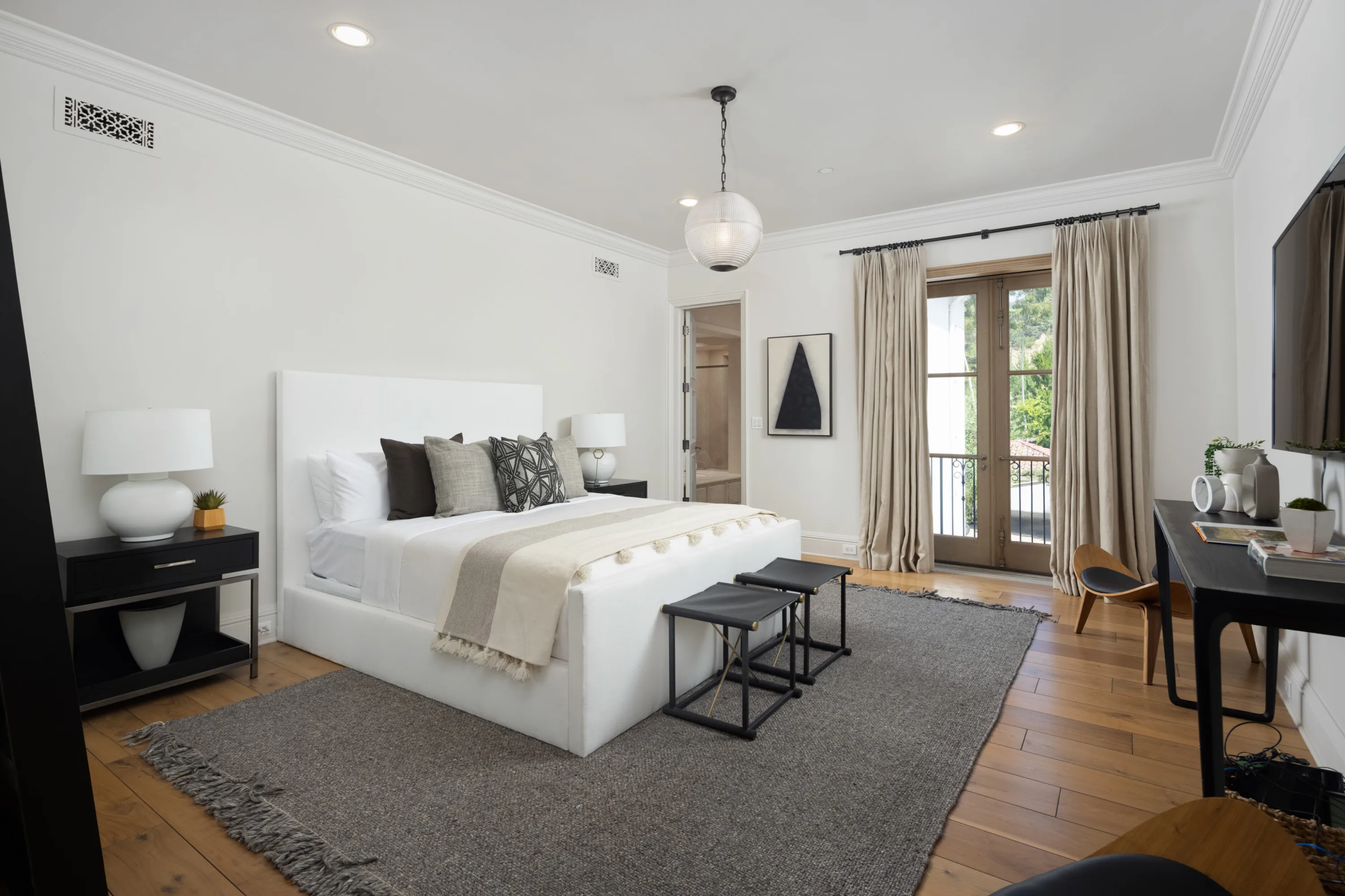 Guest bedroom in white with french doors to a small balcony and a desk facing the bed