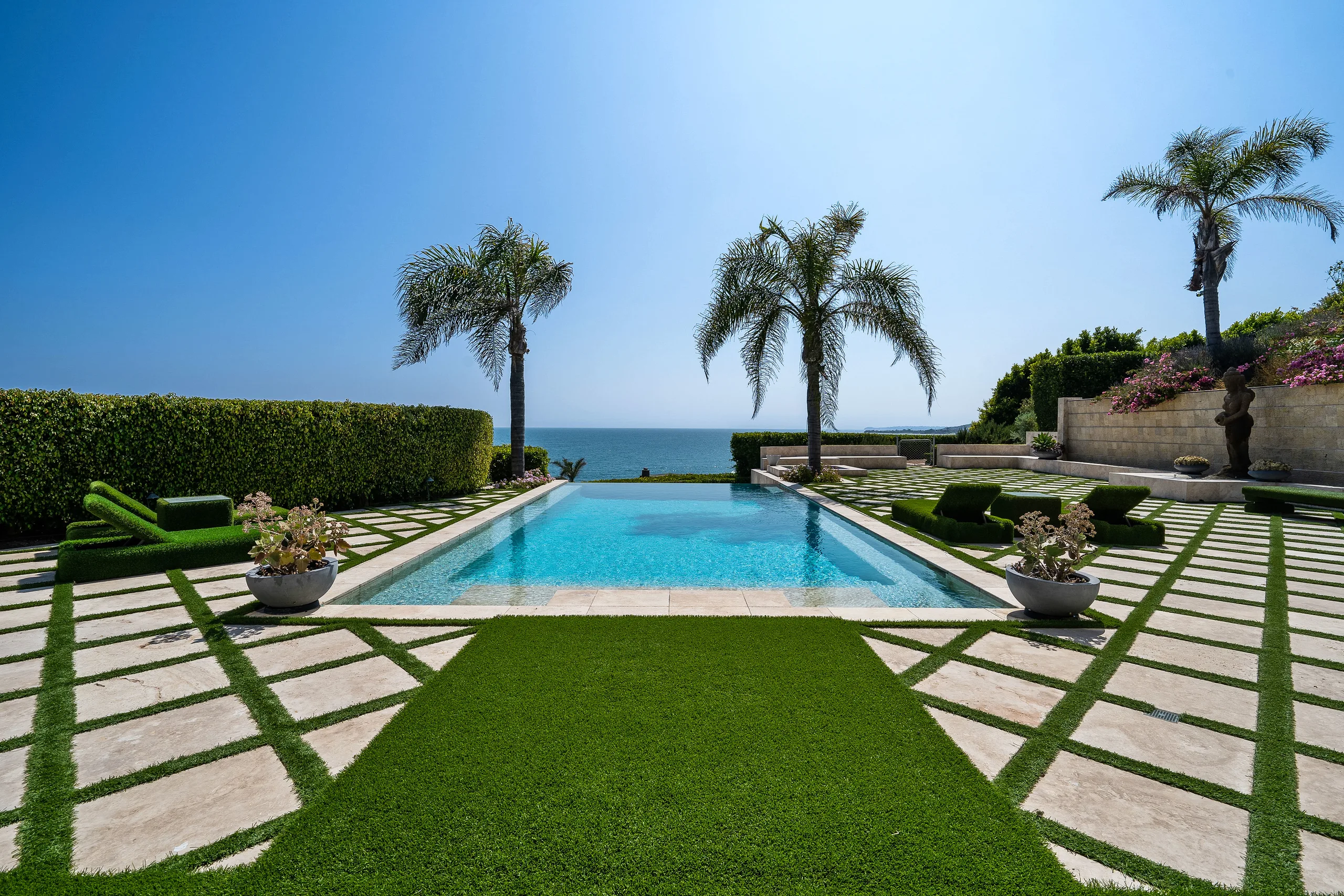 Infinity pool edged with turf-inlaid stone and palms, water meeting the Malibu coastline