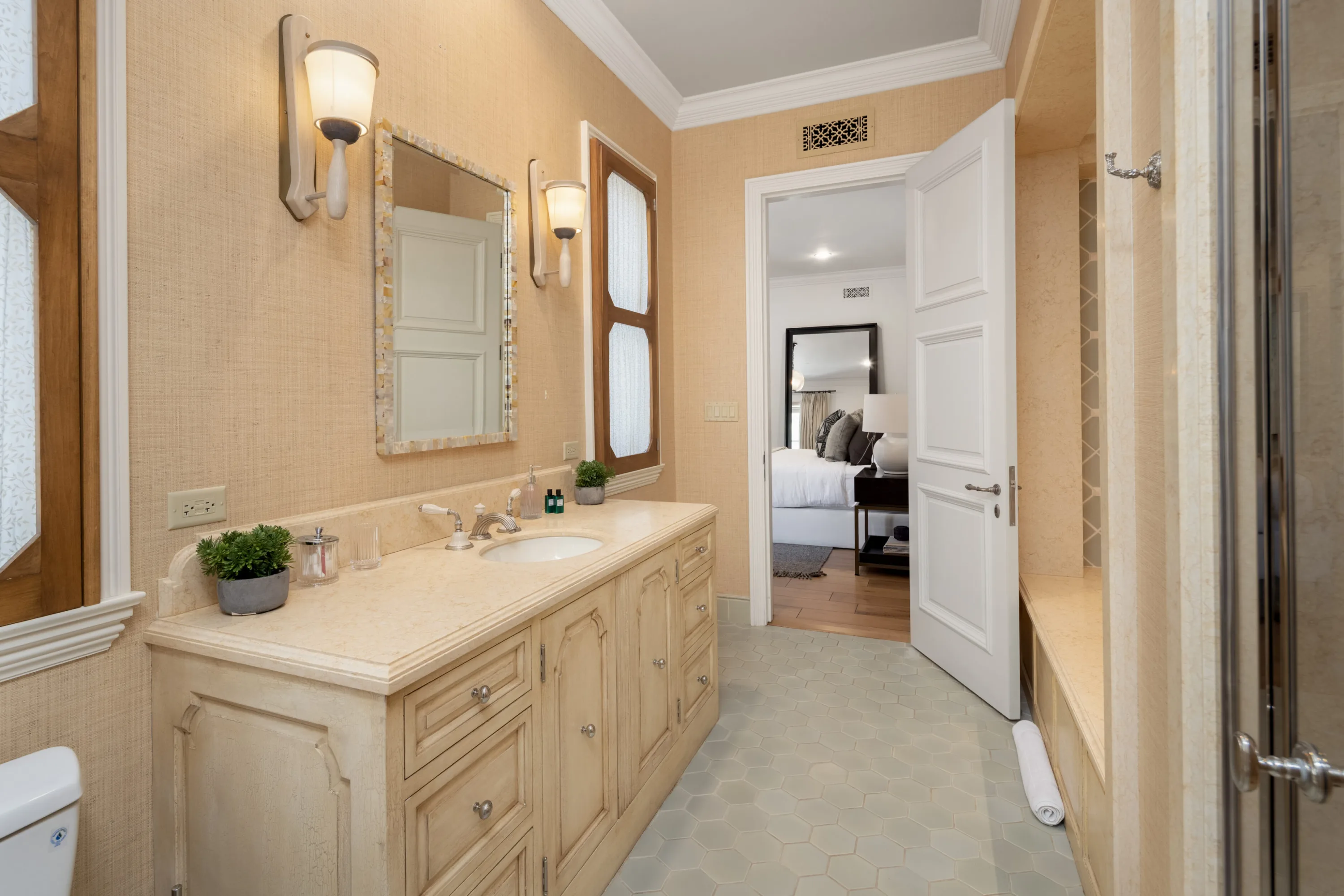 Ensuite bath with limestone vanity and shell-framed mirror, door open to the bedroom