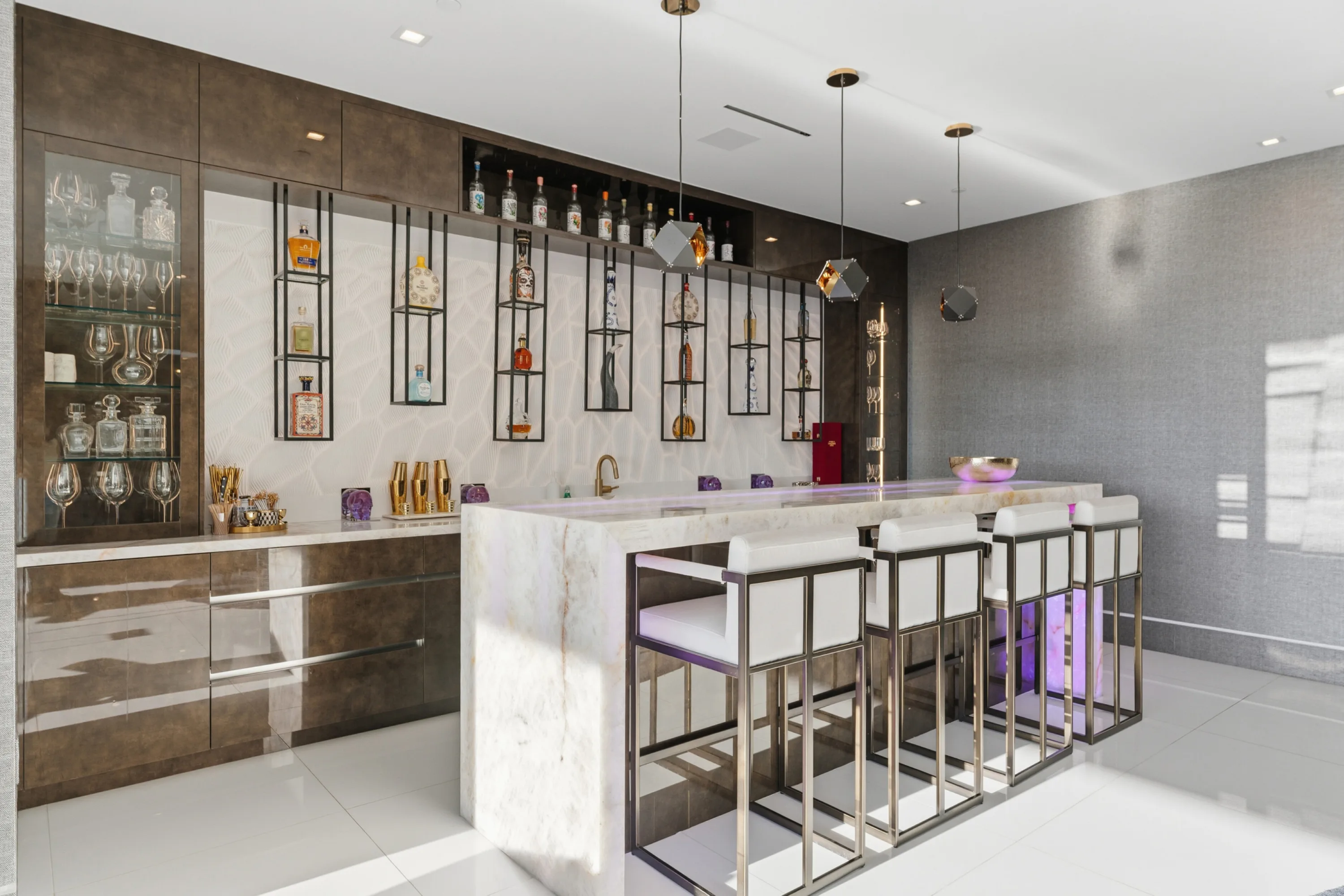 Full length of the entertaining bar, decanters in lit cabinetry and glowing stone counter