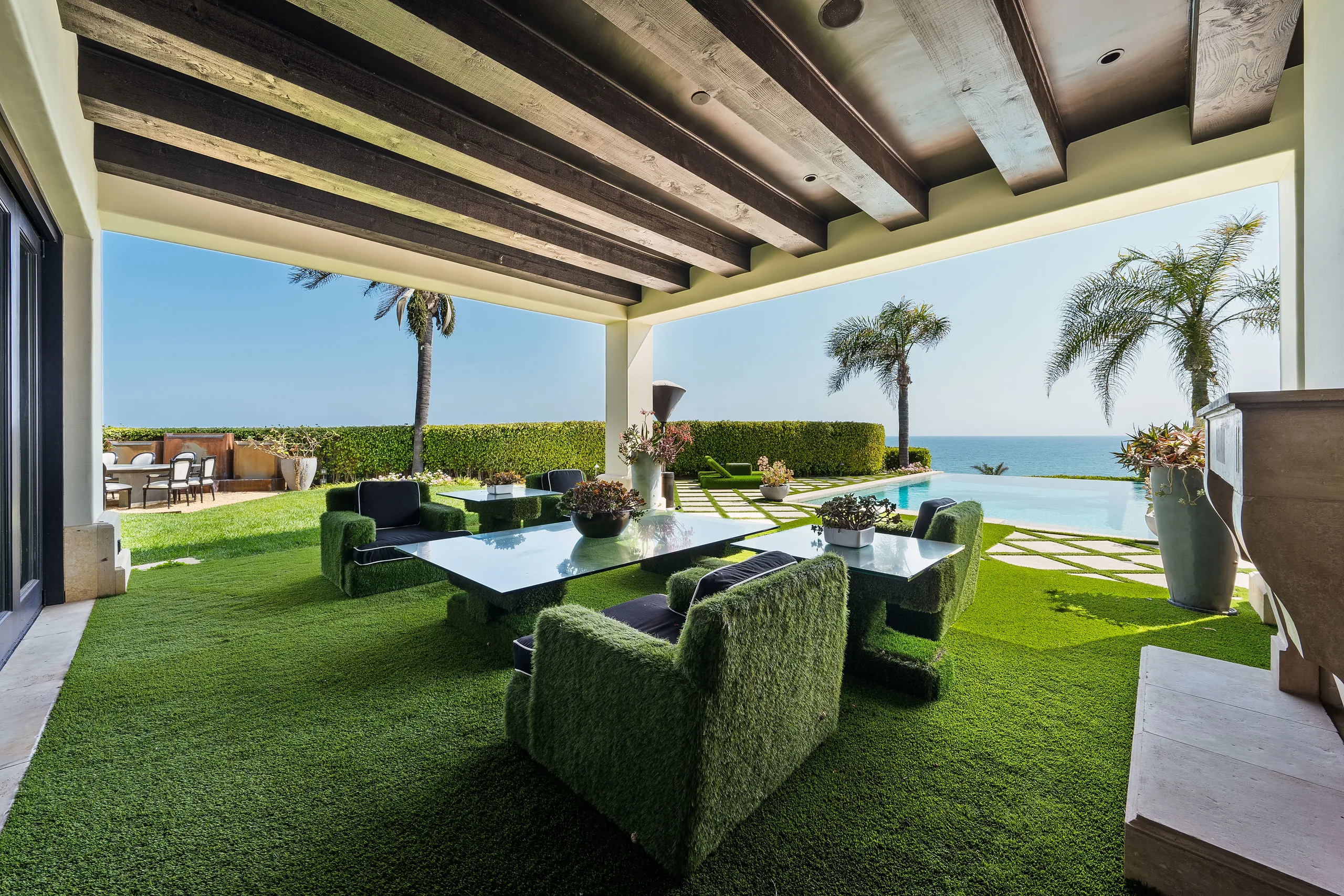 Covered beam-ceilinged lounge with grass-clad armchairs looking past the pool to open sea