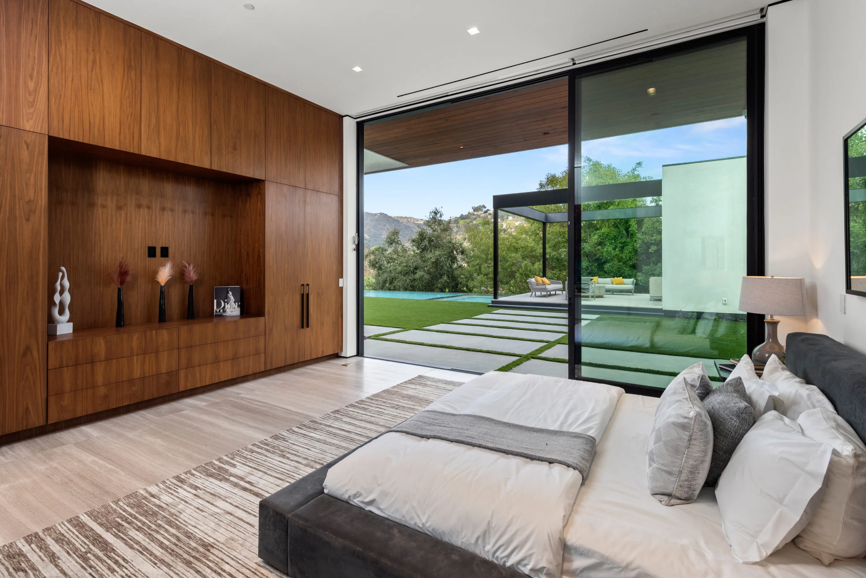 Ground-floor bedroom opening to lawn, pool and shaded lounge pavilion with the hills behind