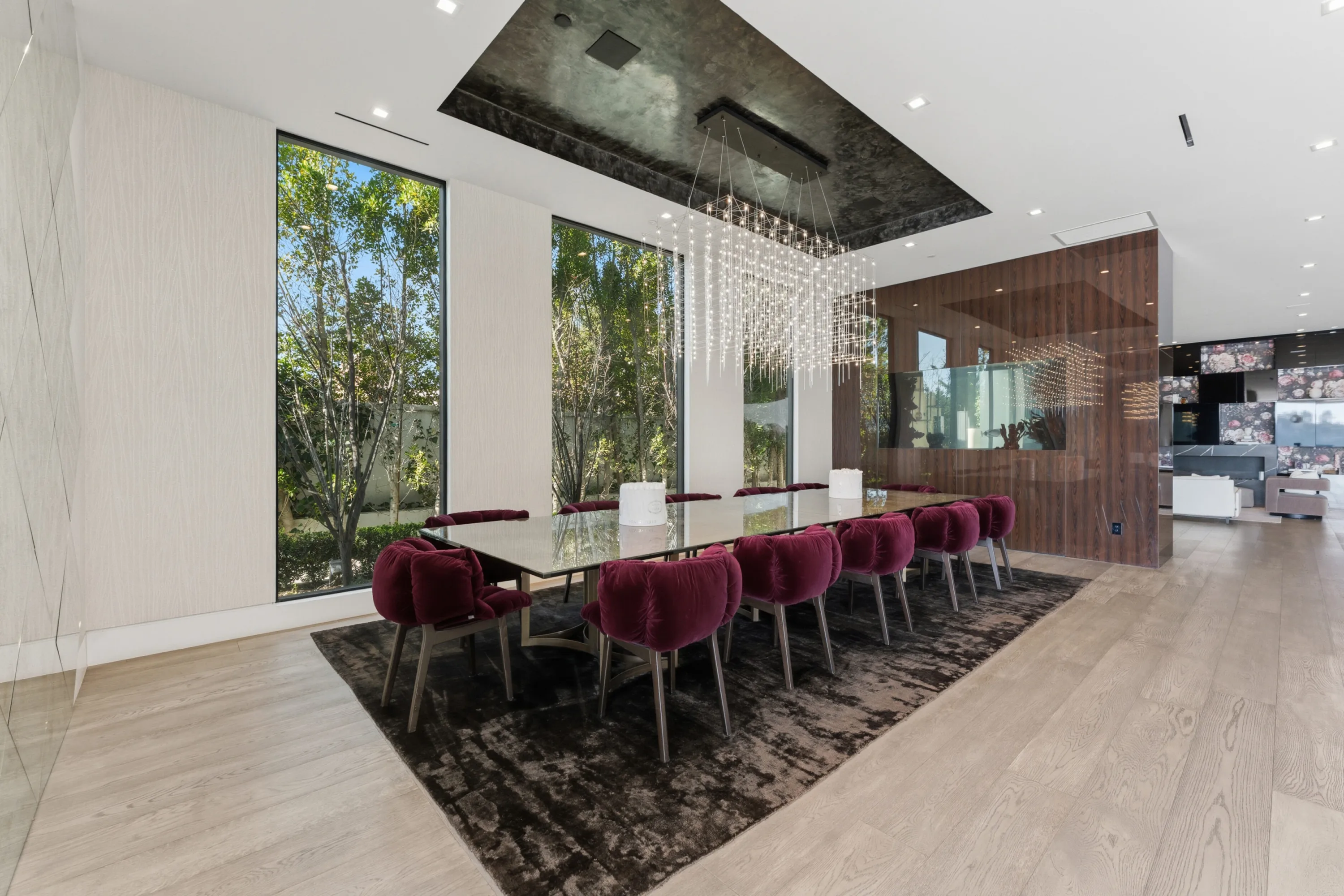 Dining room for twelve in burgundy velvet chairs beneath a cascading crystal chandelier, tall windows onto the birch garden