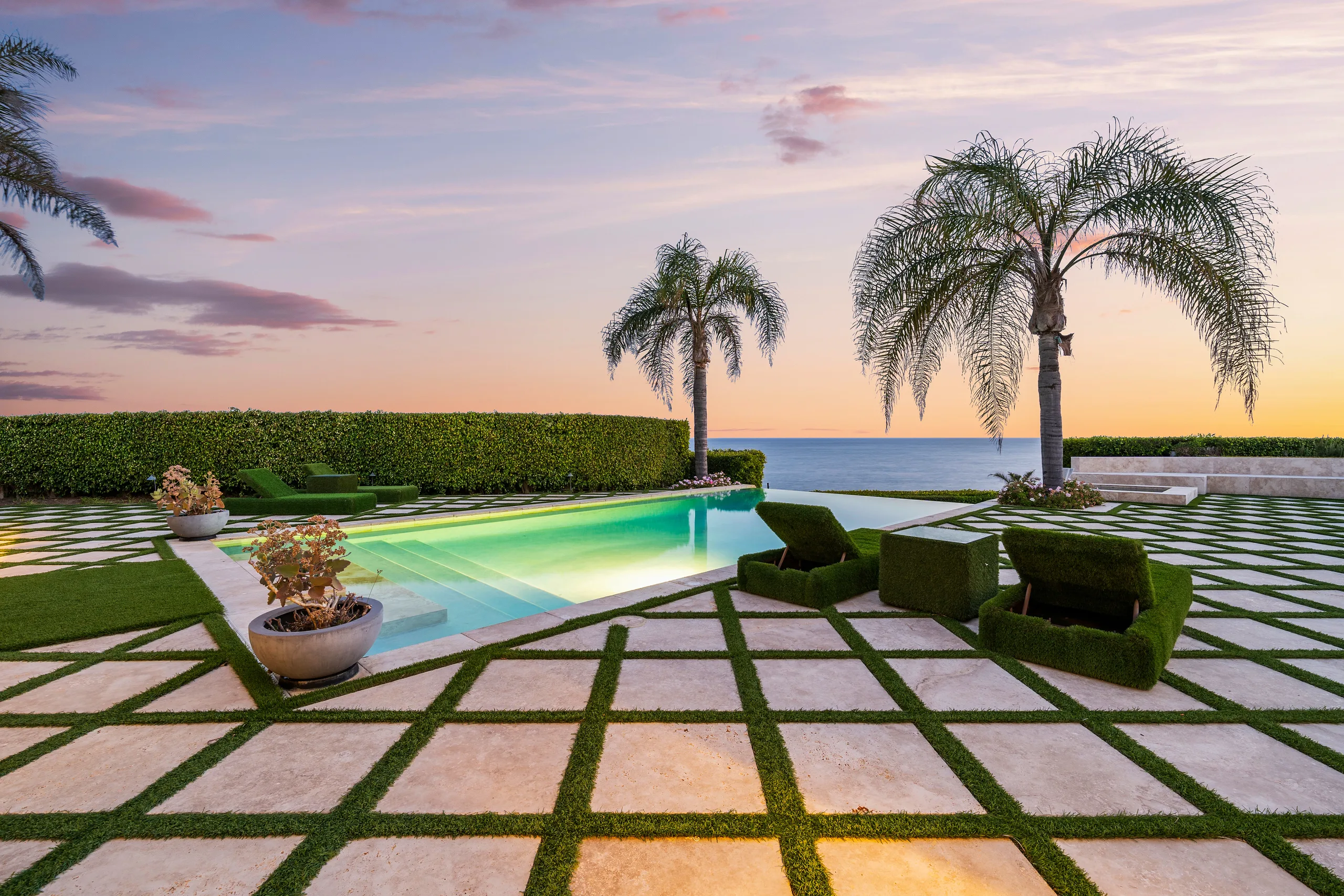 Infinity pool edged in turf-covered loungers, palms silhouetted against a pink and amber Malibu sunset