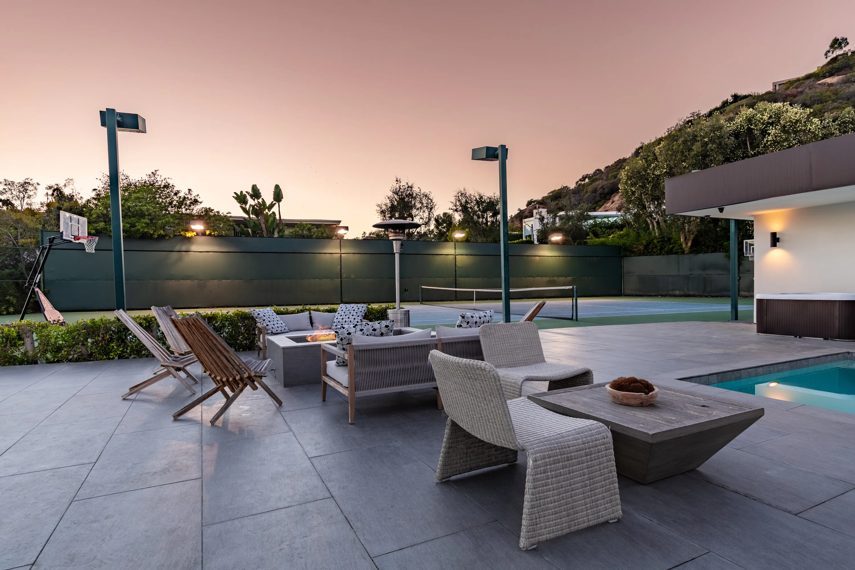 Fire pit seating group on the pool deck looking toward the floodlit tennis and basketball court