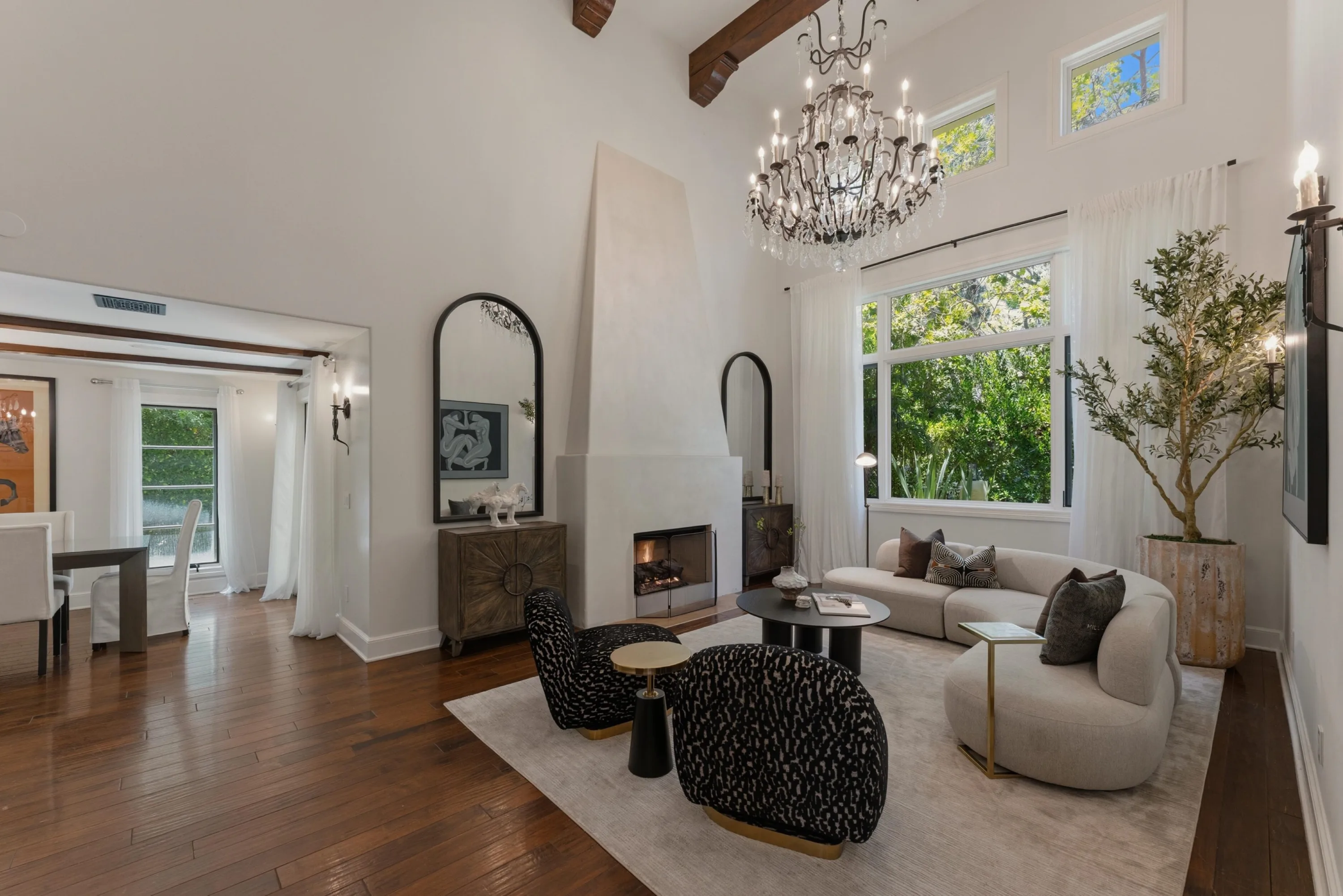Formal living room with plaster fireplace, crystal chandelier and curved sofa under beamed ceiling
