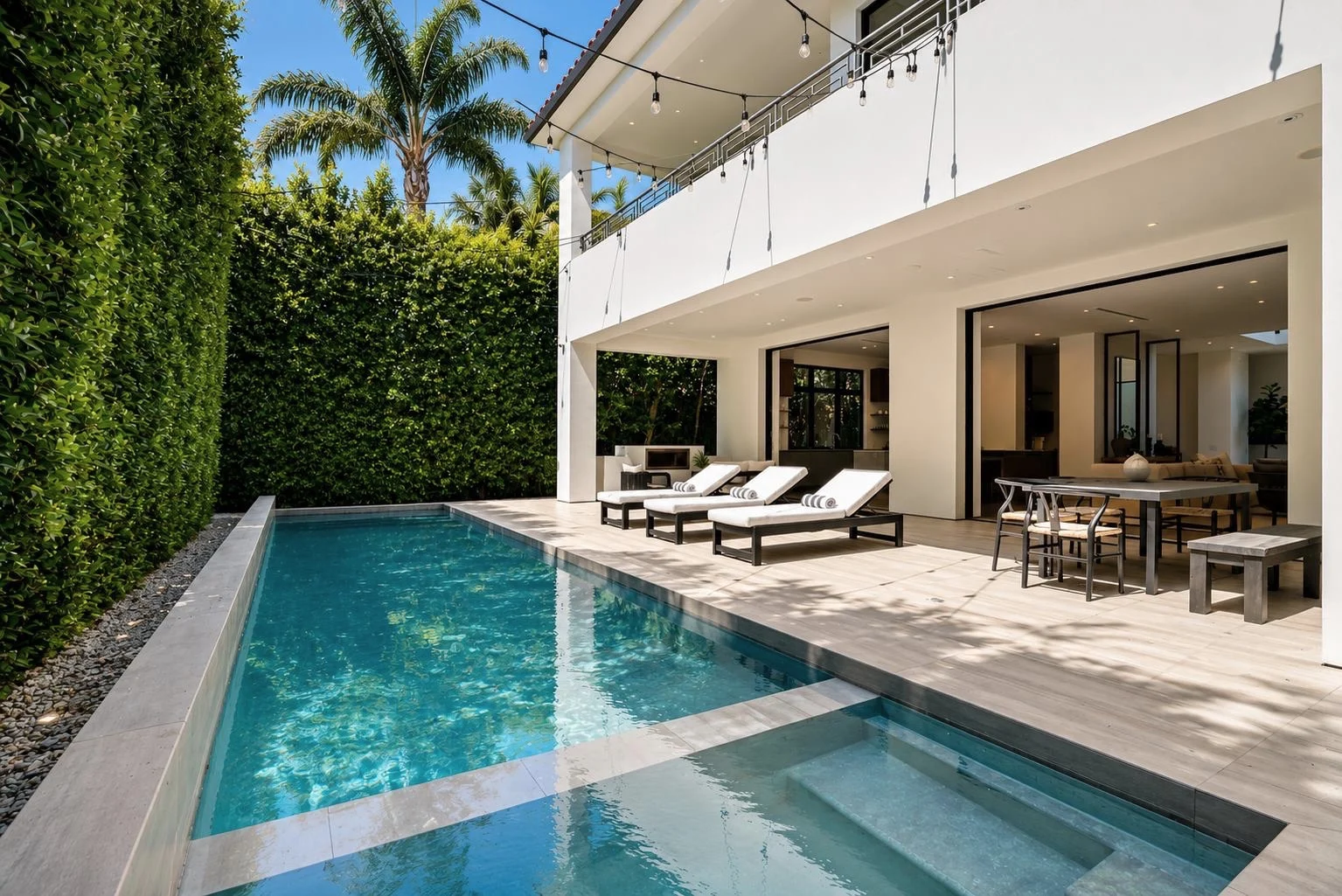 Hedge-screened pool and spa with sun loungers, festoon lights and a shaded dining terrace