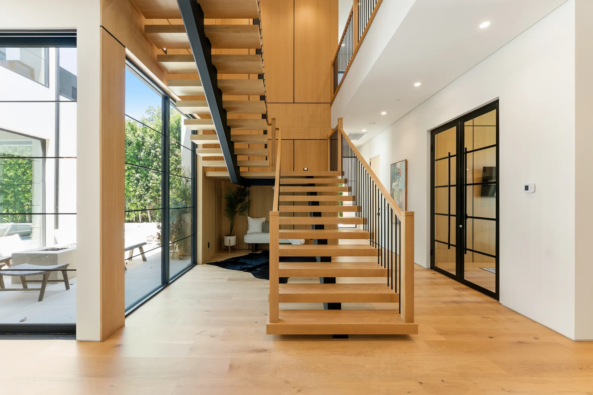 Double-height stair hall with floating oak treads, black steel glazing and a garden view