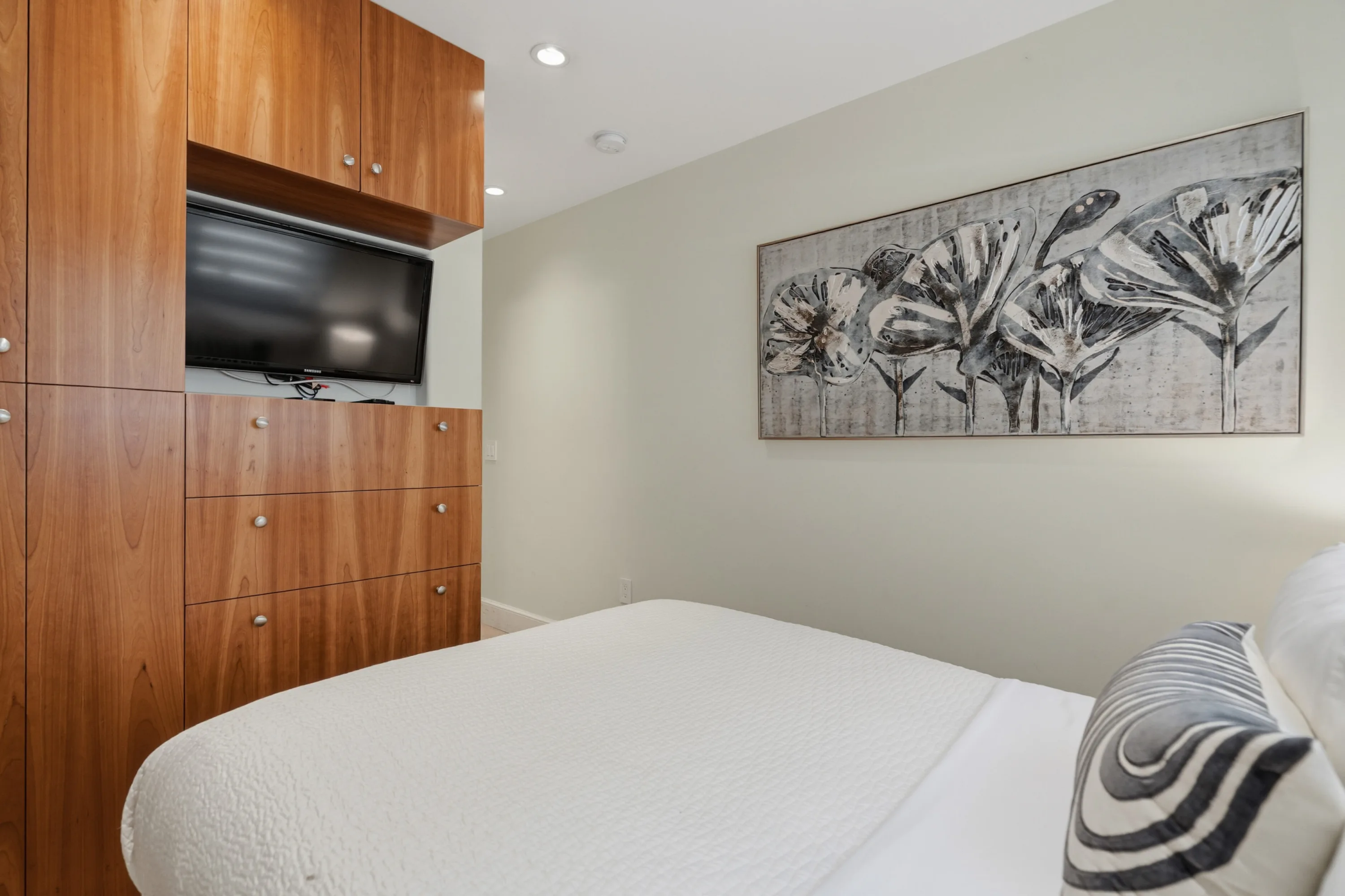 Bedroom's built-in wood wardrobe wall with recessed television, beside an oversized floral artwork