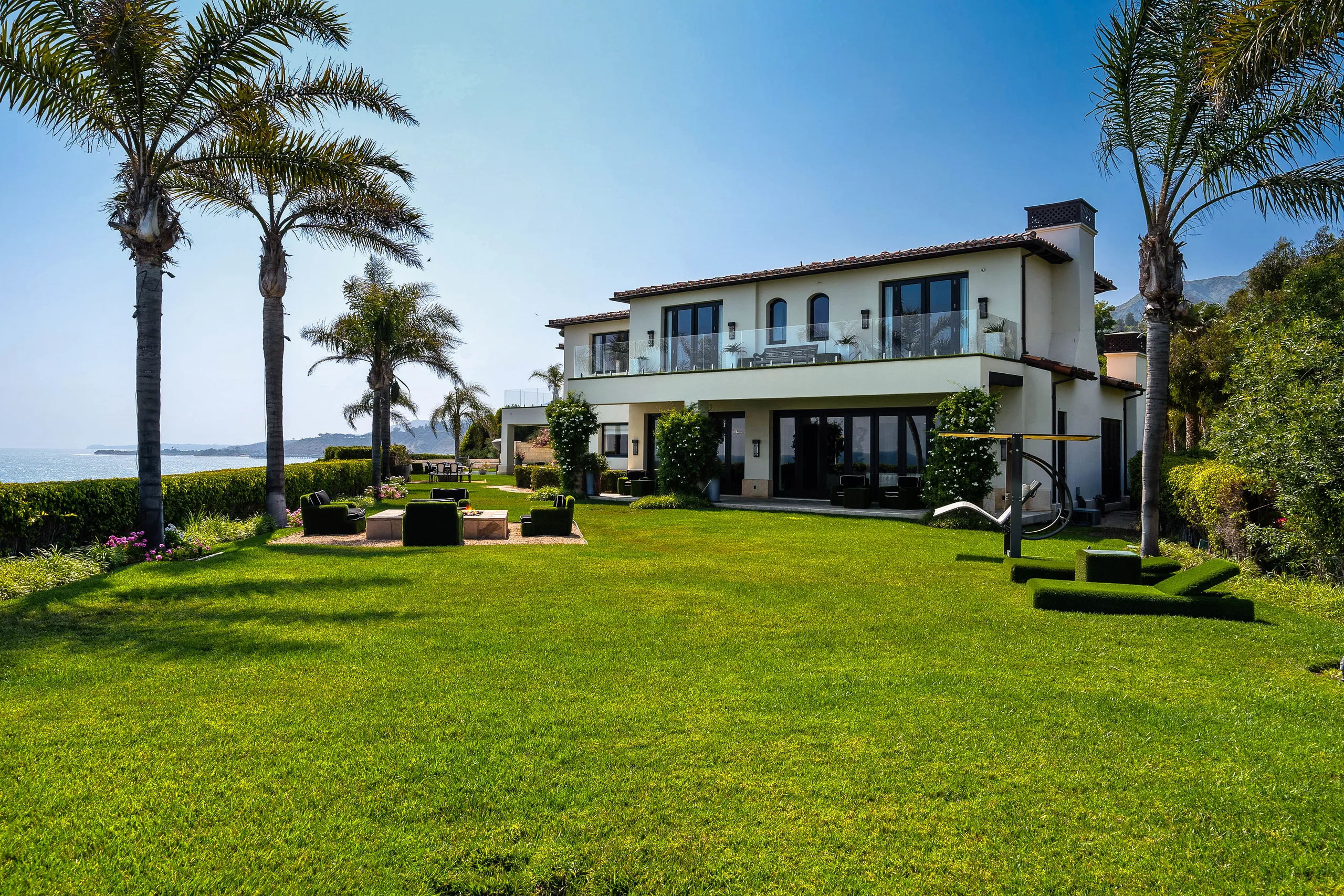 Rear elevation across the lawn, with fire-pit seating, glass balcony and ocean to one side