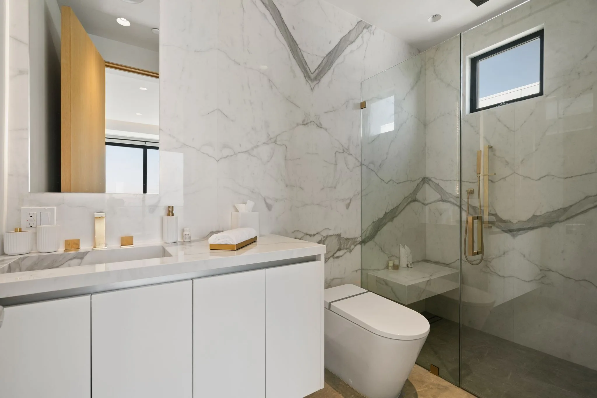 Bathroom lined in book-matched white marble with brass fixtures and a bench in the walk-in shower