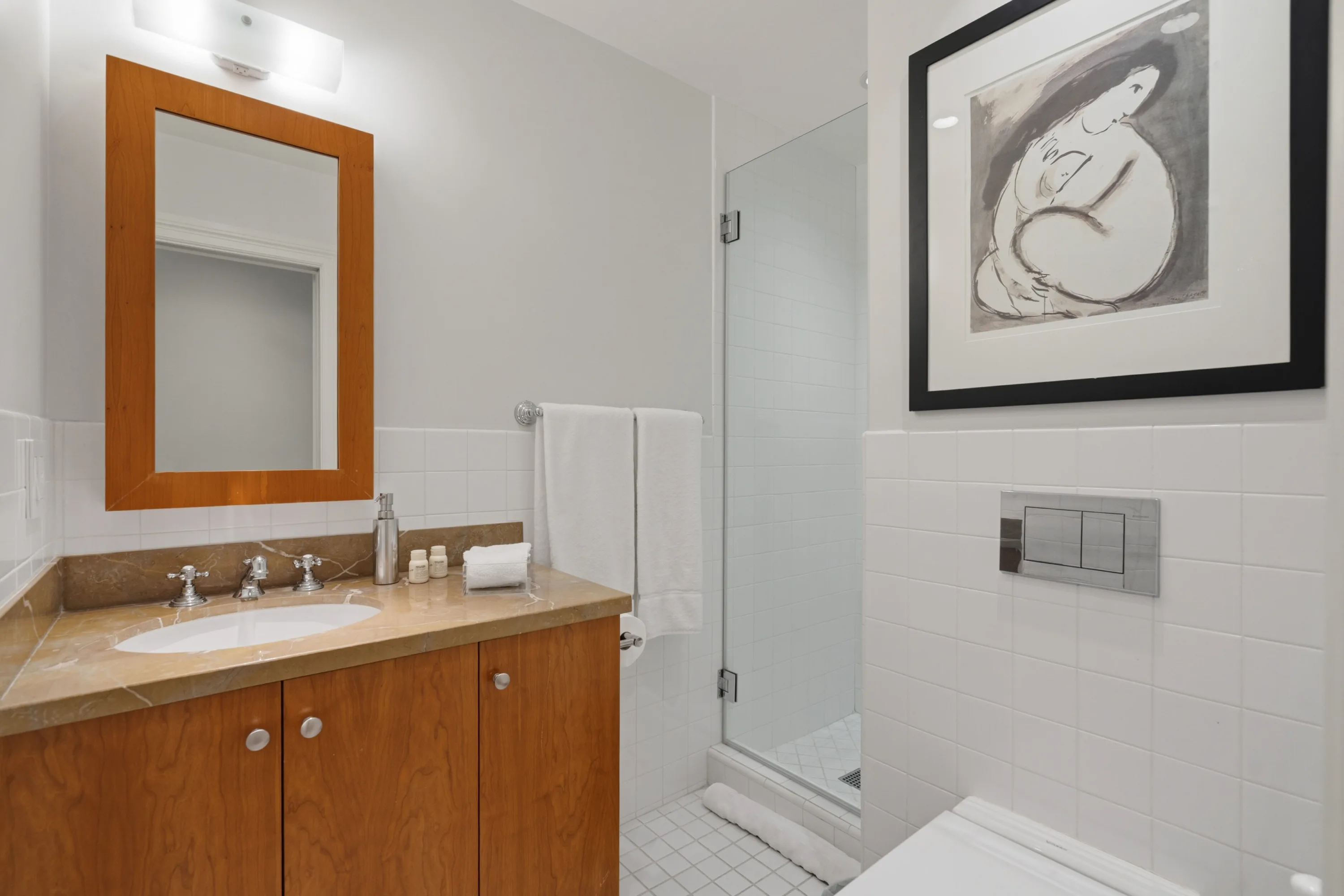 Second guest bath with marble-topped vanity, glass shower stall and a framed charcoal figure study