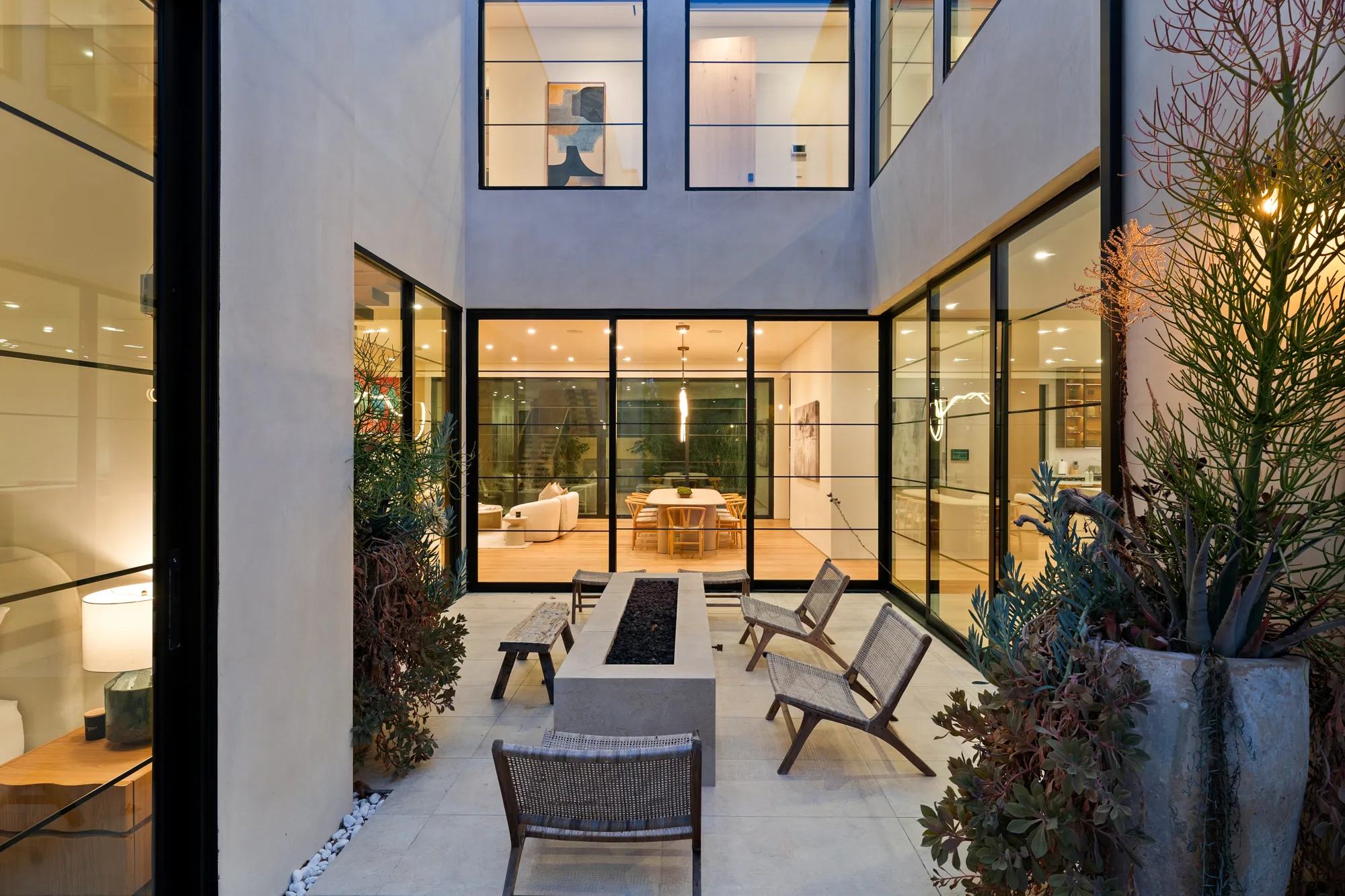 Evening in the glazed courtyard, fire table alight and the dining room and kitchen glowing through the glass