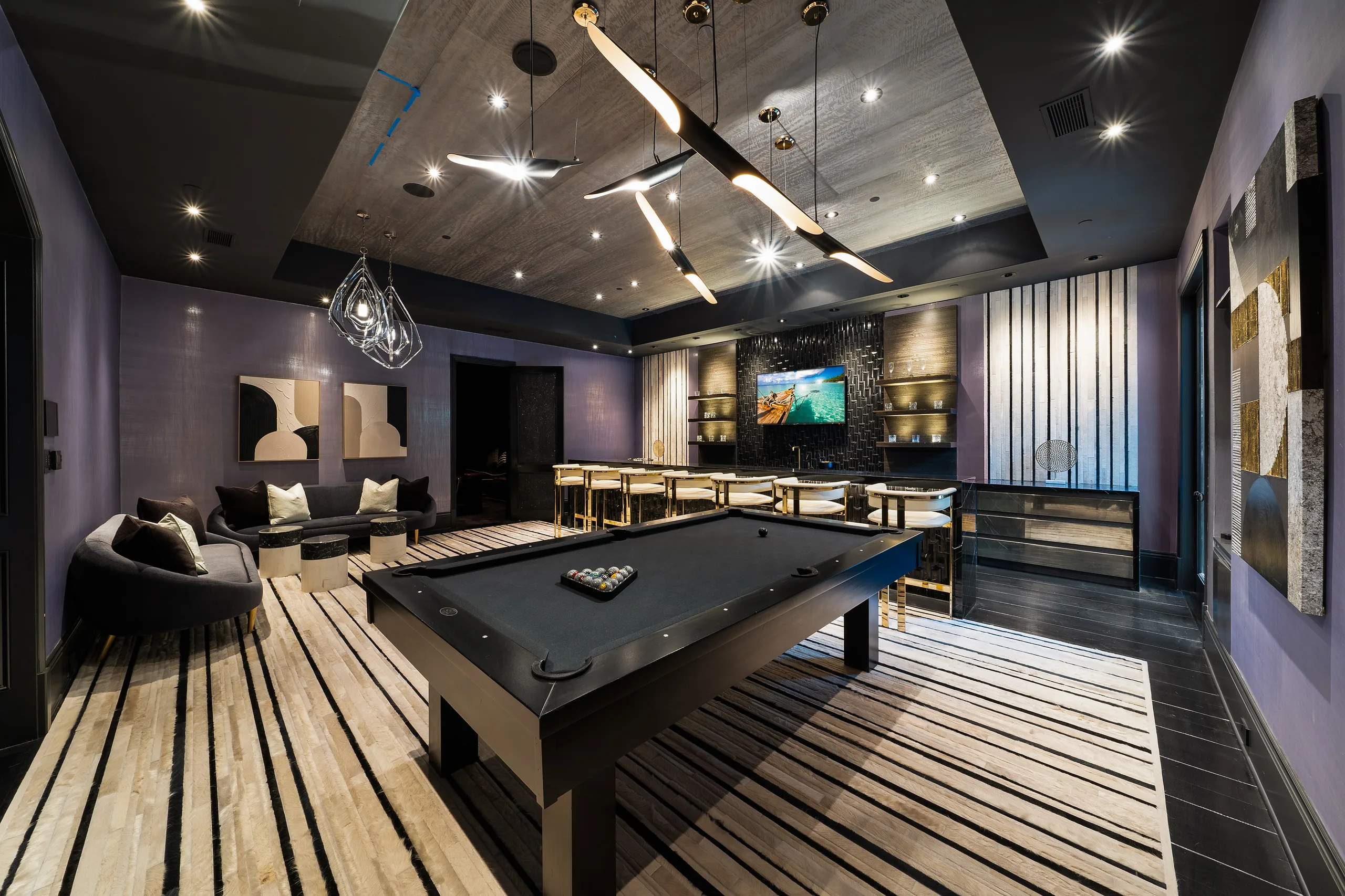 Games room in plum tones with pool table, bar seating for eight and sculptural lighting