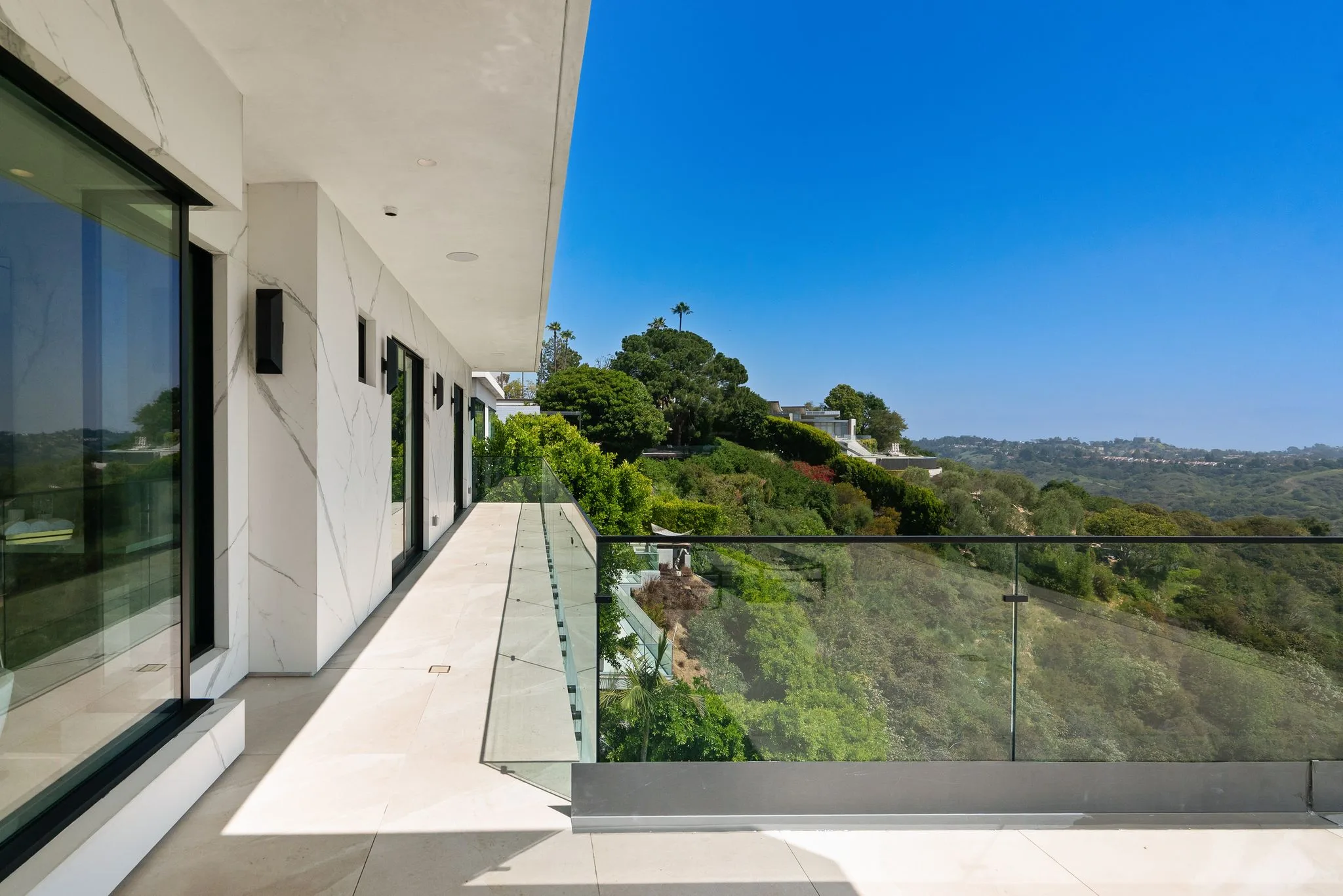 Wraparound balcony along the marble-clad facade, glass railing framing the wooded Bel Air hillside