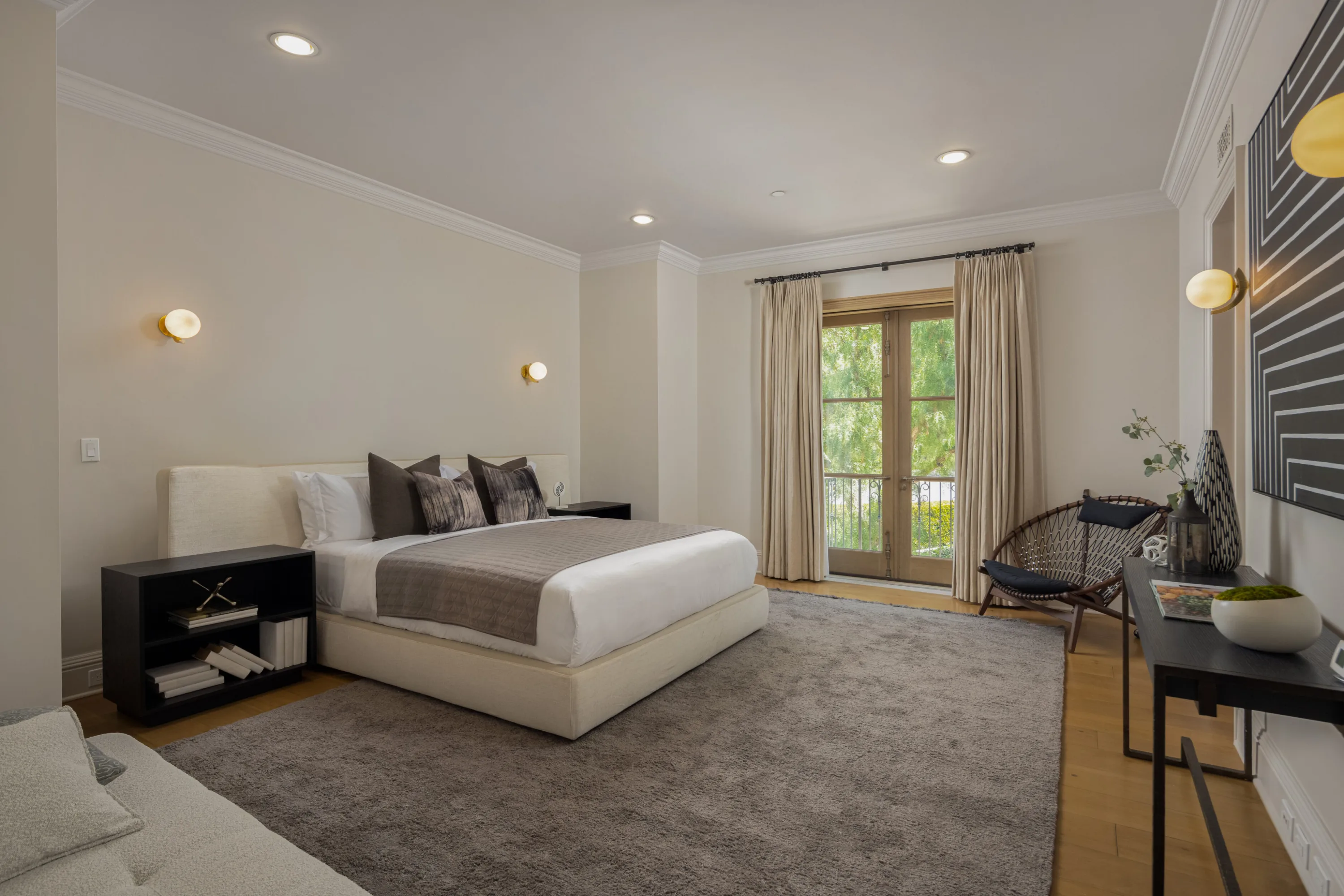Calm guest bedroom with plush grey rug and french doors onto a leafy balcony