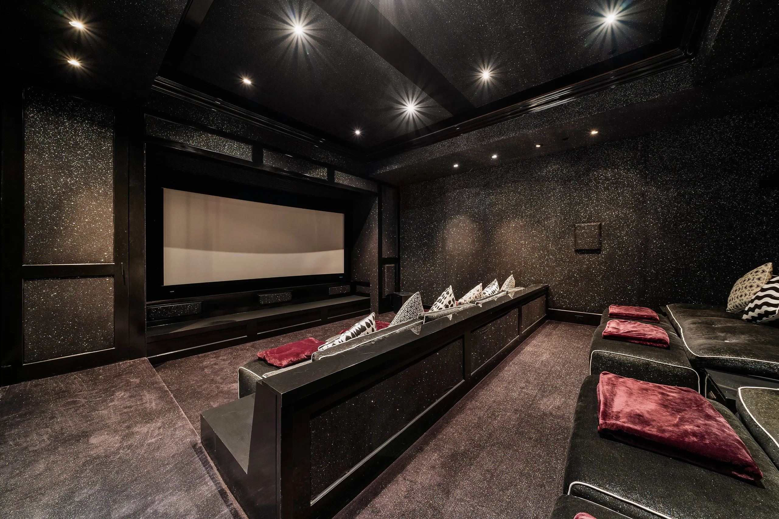 Tiered home cinema in glitter-black finish with velvet recliners and red throws facing the screen