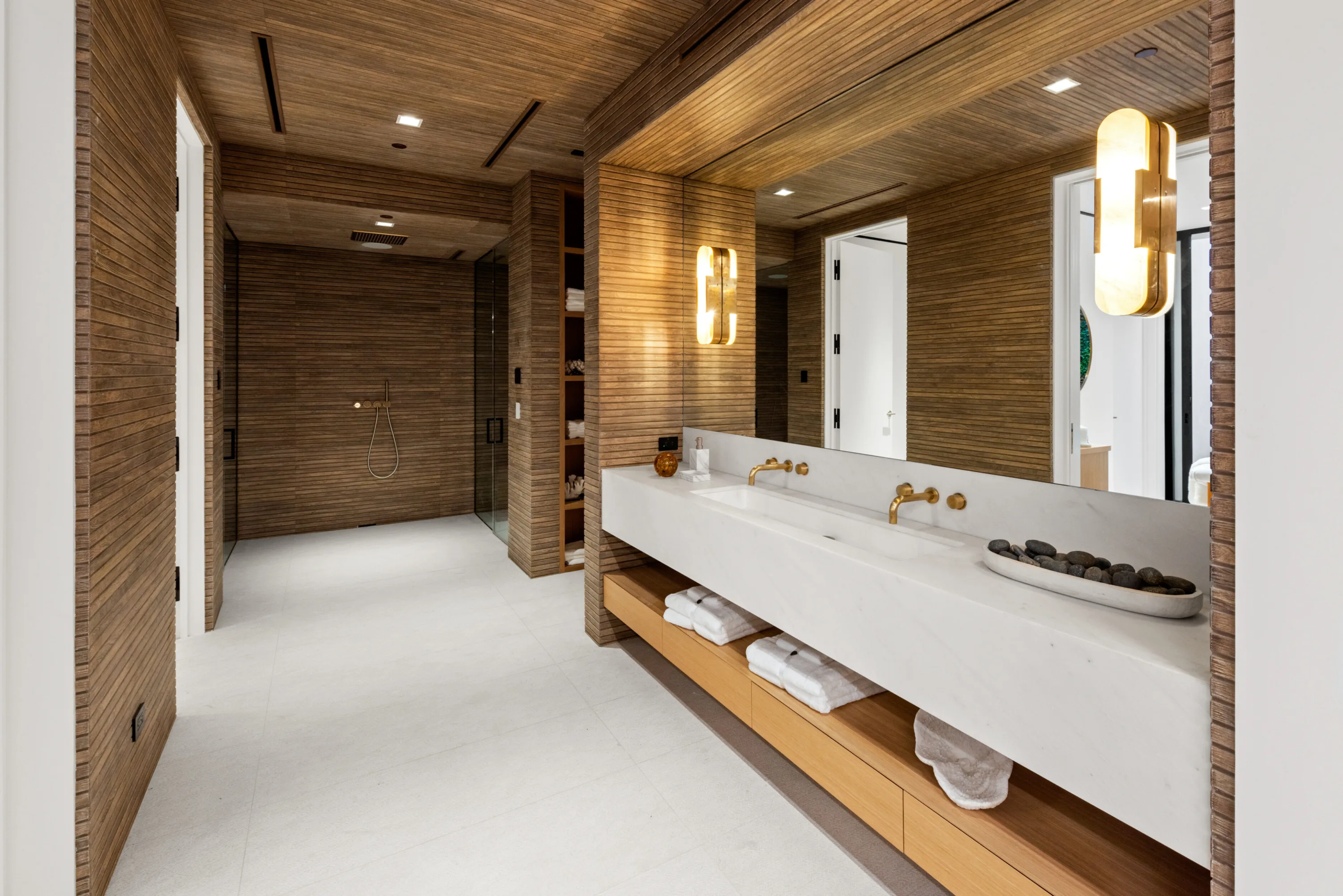 Spa bath lined in slatted timber, long stone double vanity with brass taps and a walk-in rain shower