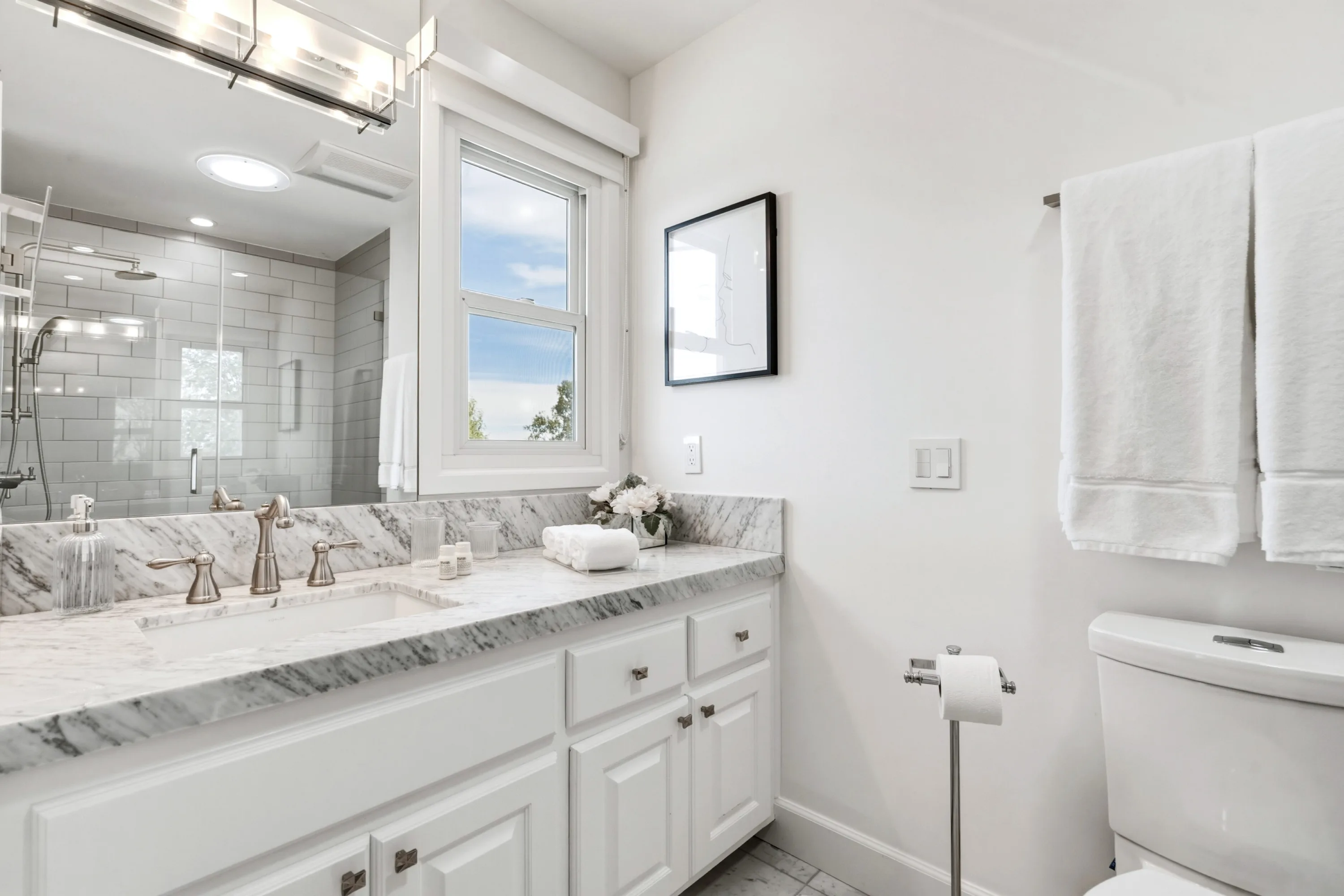 Guest bath with marble vanity, wide mirror reflecting the tiled shower, and stacked white towels