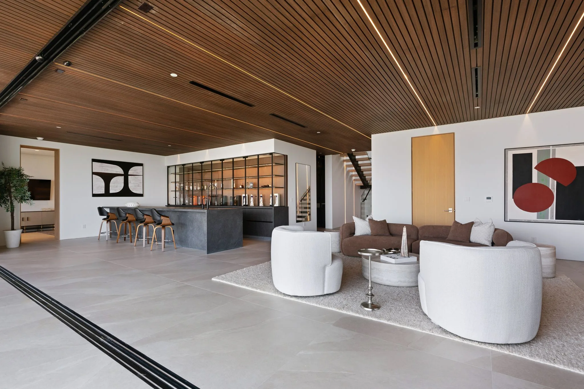 Open great room under a slatted walnut ceiling, with bar seating and curved lounge chairs