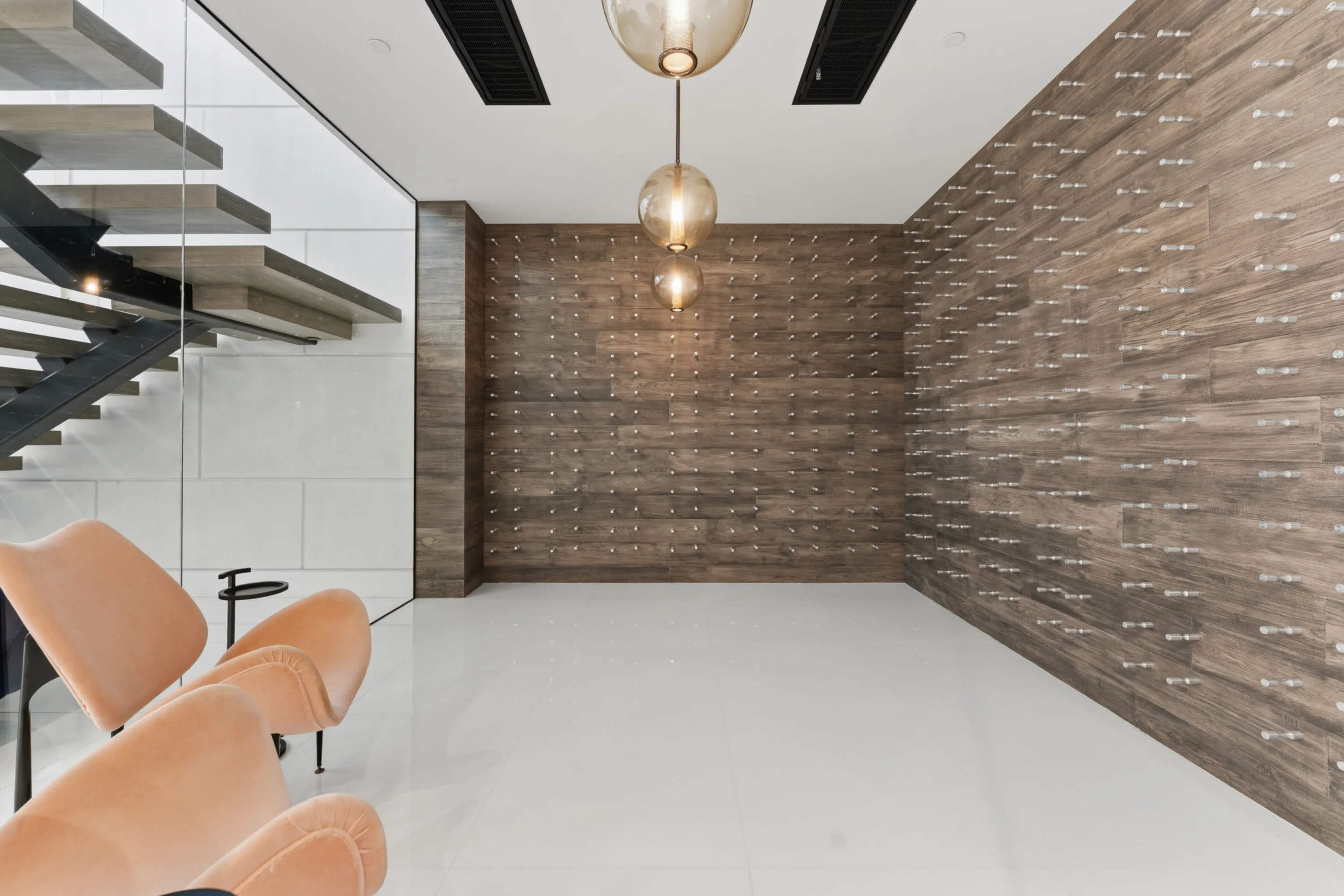 Climate-controlled wine room with wood-clad display walls, glass globe pendants and velvet lounge chairs