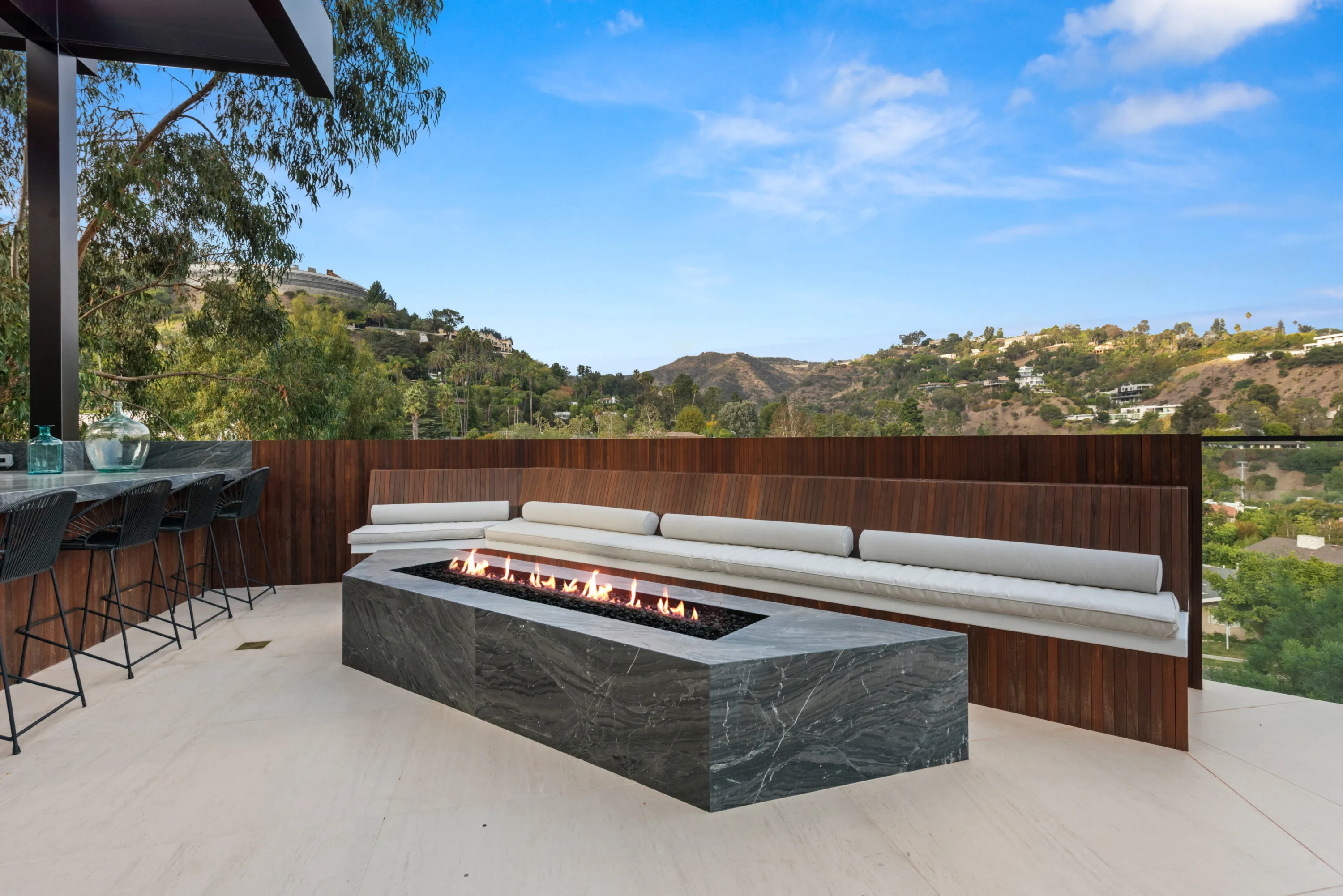 Rooftop terrace with a linear stone fire table, banquette cushions and bar stools facing the canyon ridgeline