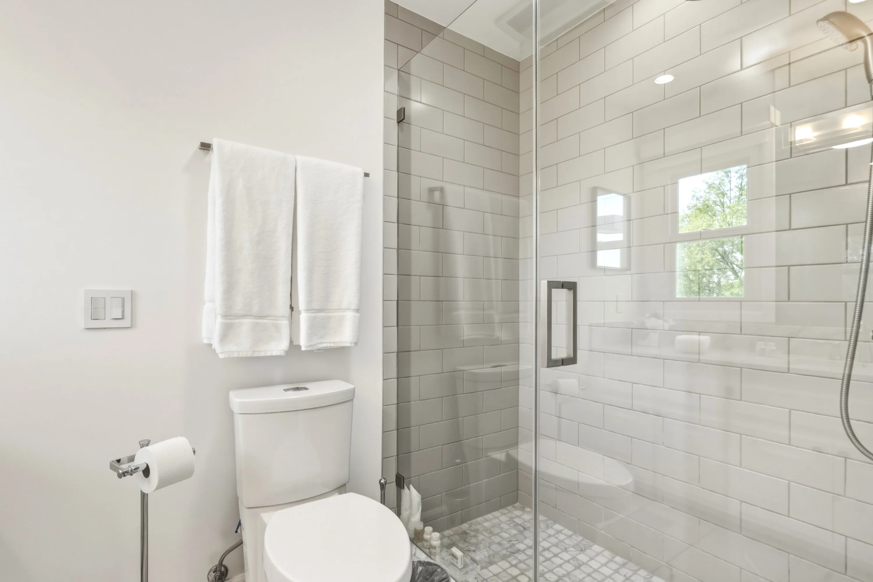 Compact ensuite with glass-enclosed shower, bench seat and folded towels on a chrome rail