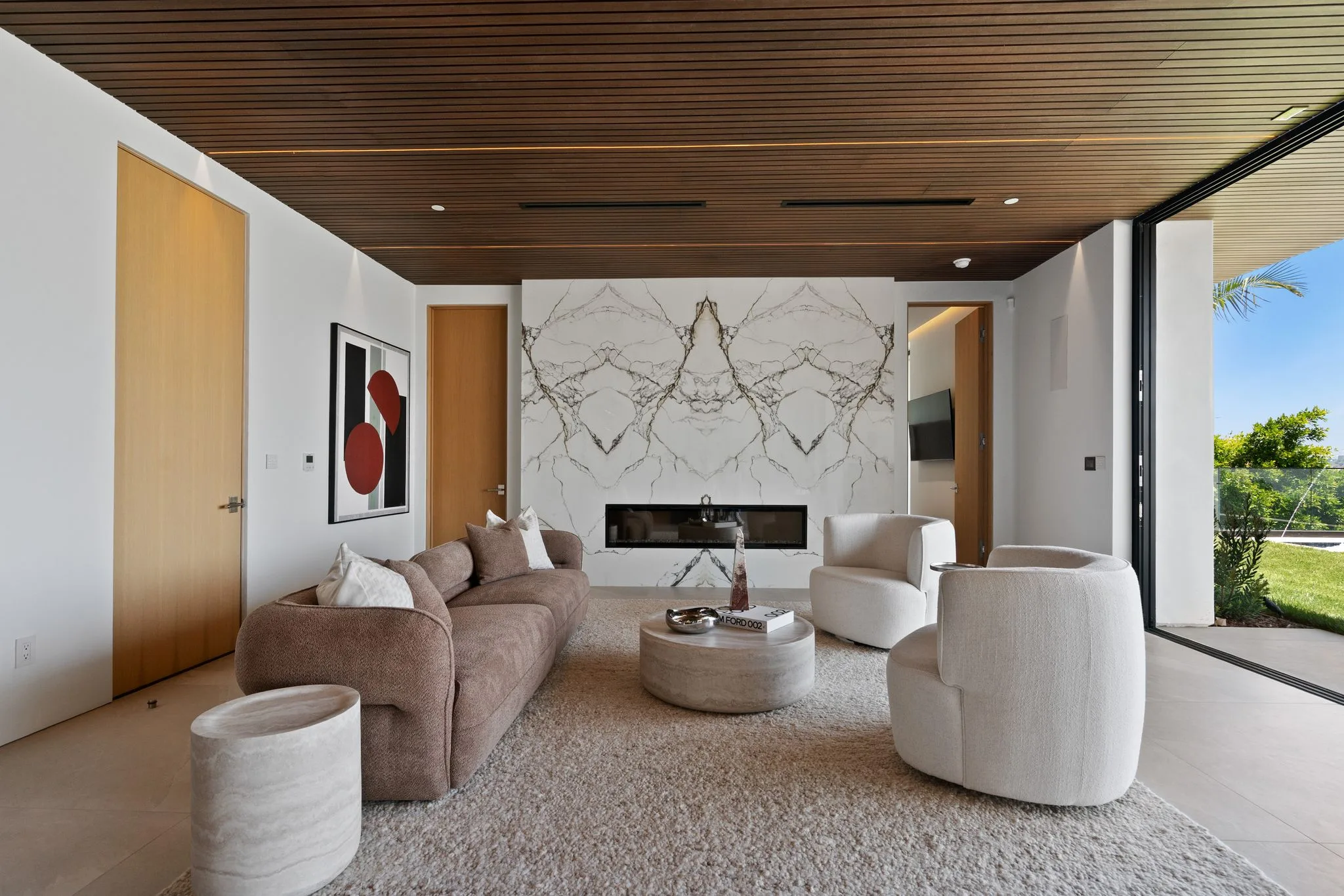 Lounge with book-matched marble fireplace wall, sculptural seating and a coffee-table book reading "Ford 002"