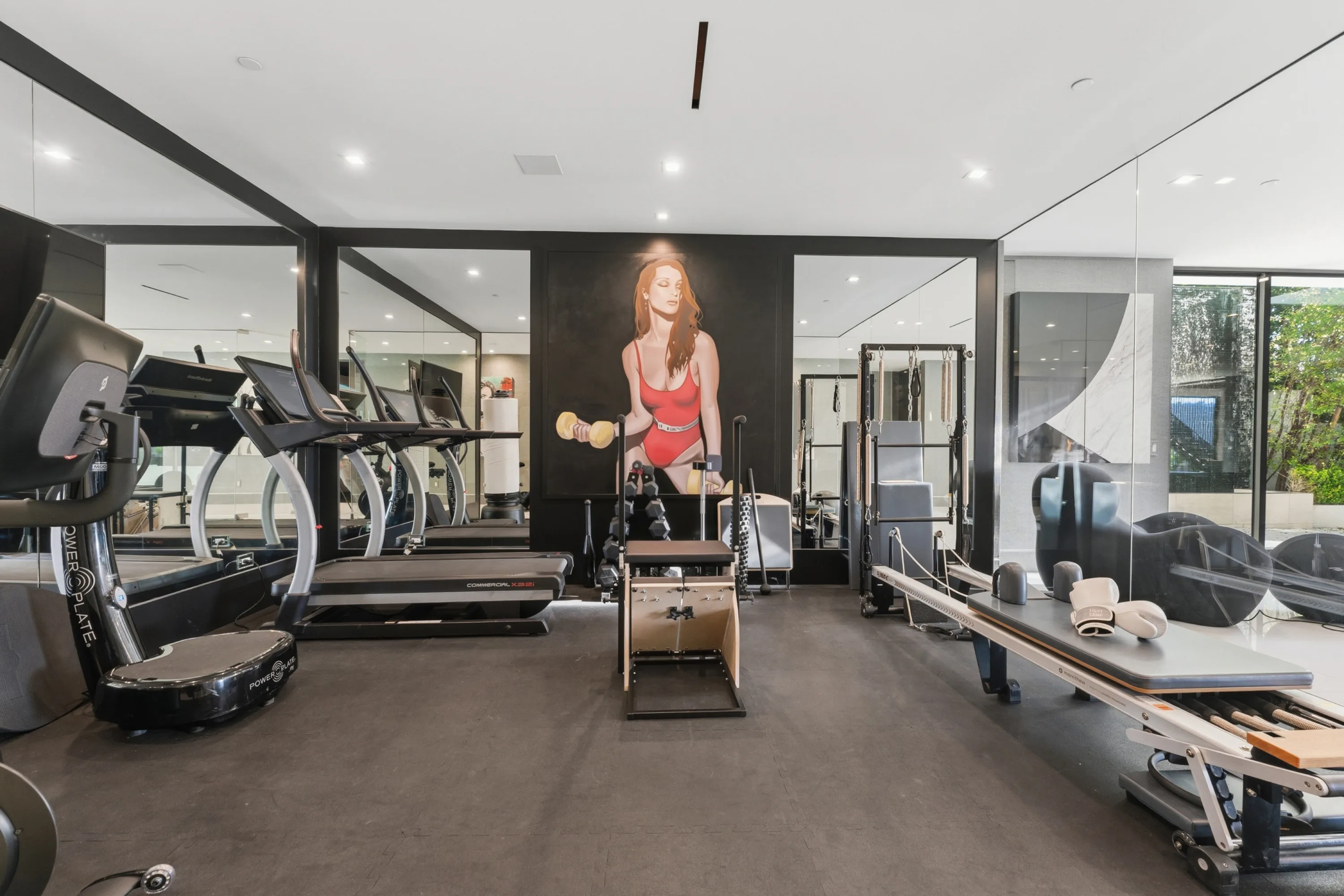 Mirrored fitness studio with treadmills, reformer, free weights and a red-swimsuit portrait on the dark feature wall