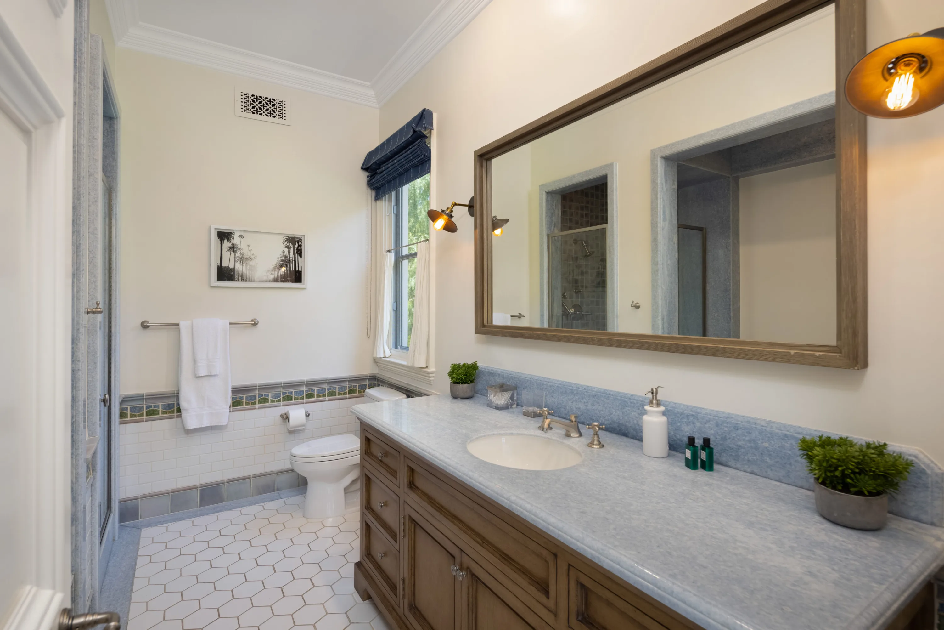Guest bath in blue and cream with timber-framed mirror and framed palm-tree photograph