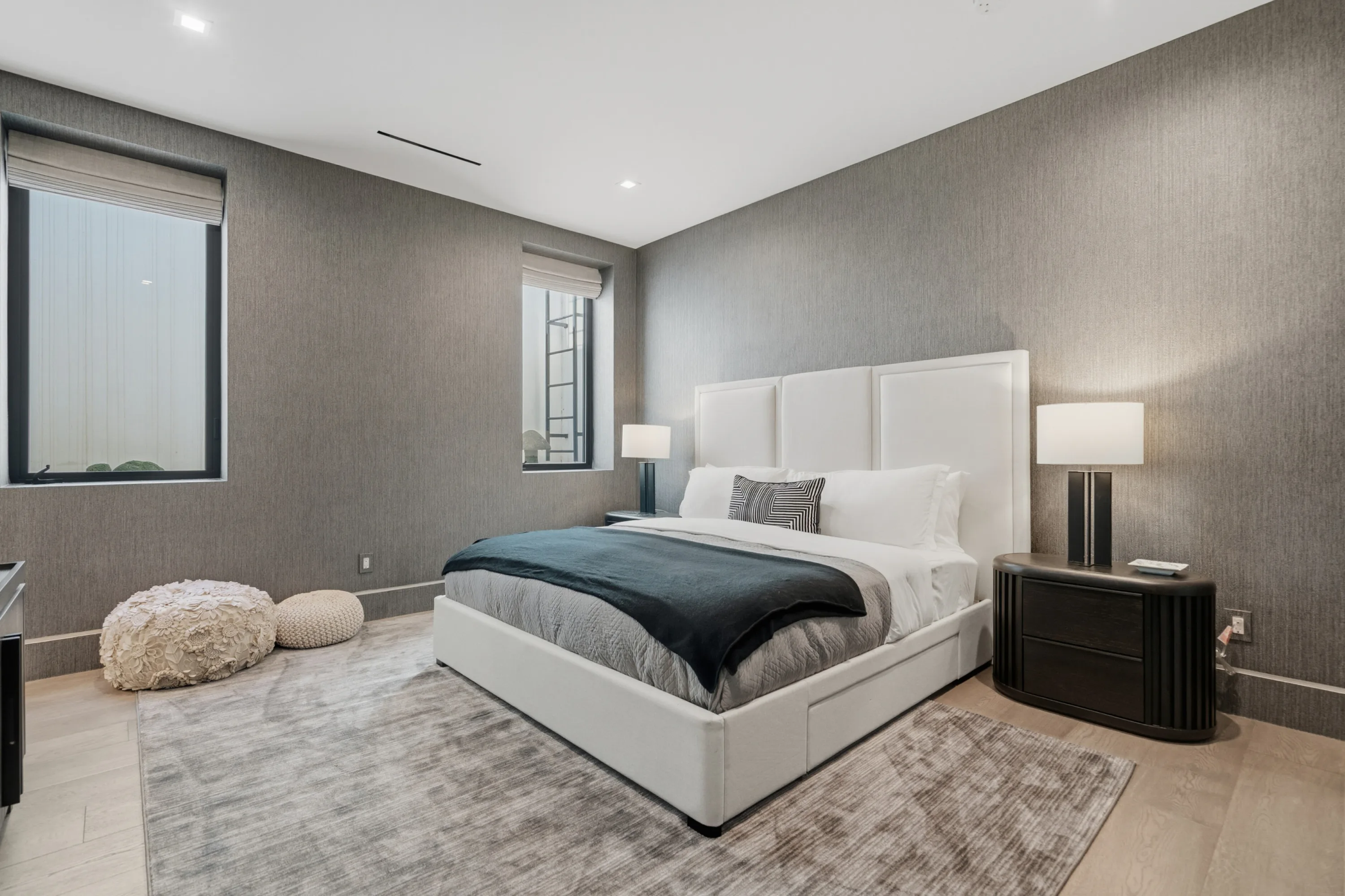 Guest bedroom with upholstered king bed, textured grey walls and warm lamplight over a soft area rug